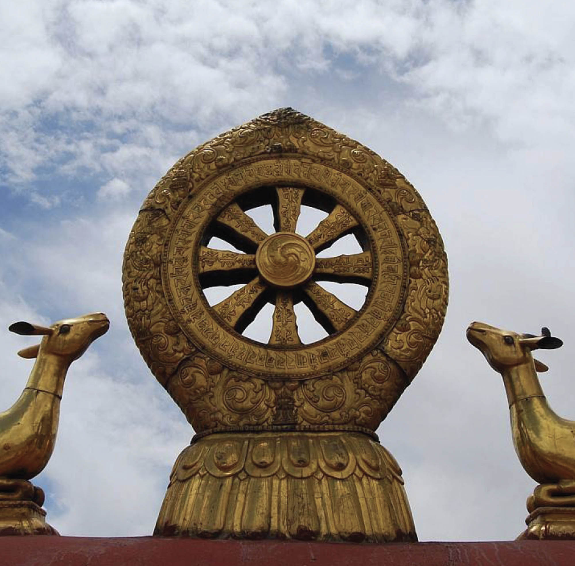 A golden sculpture of an 8-spoke wheel carved with symbols. On either side of the wheel is a sculpture of an animal facing the wheel.