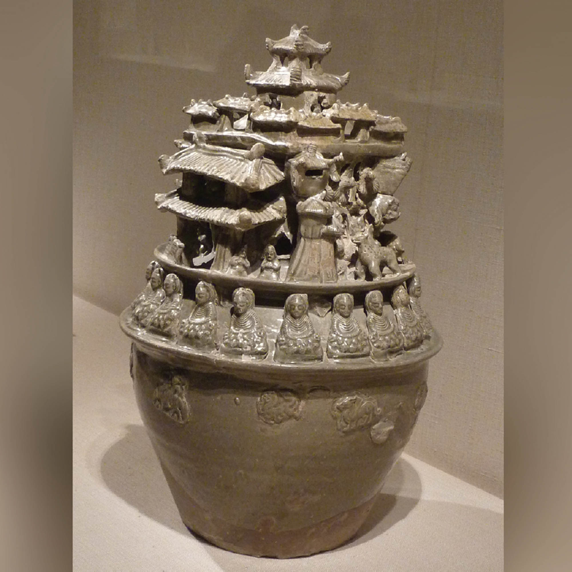 Extremely ornate jar features carving s and sculptures all around the top of it. There is a row of seated Buddhas, as well as a temple.