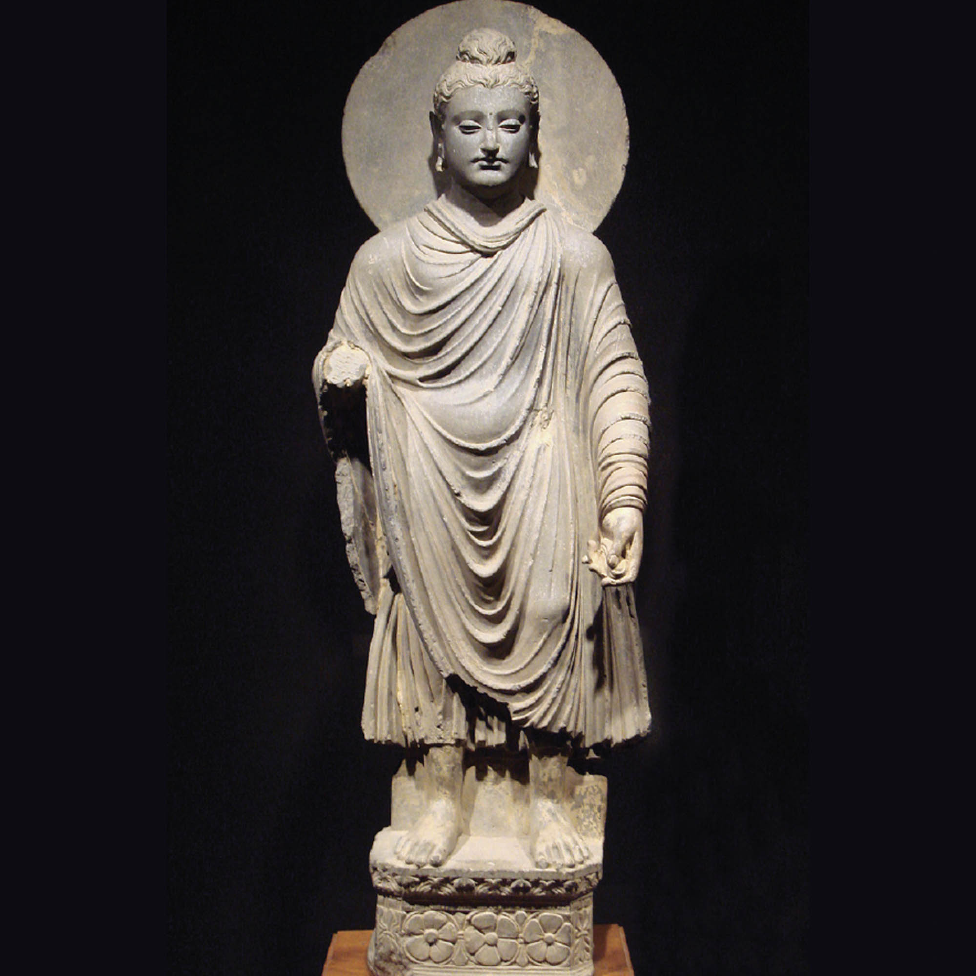 A sculpture of a Buddha standing, wearing draped, long robes