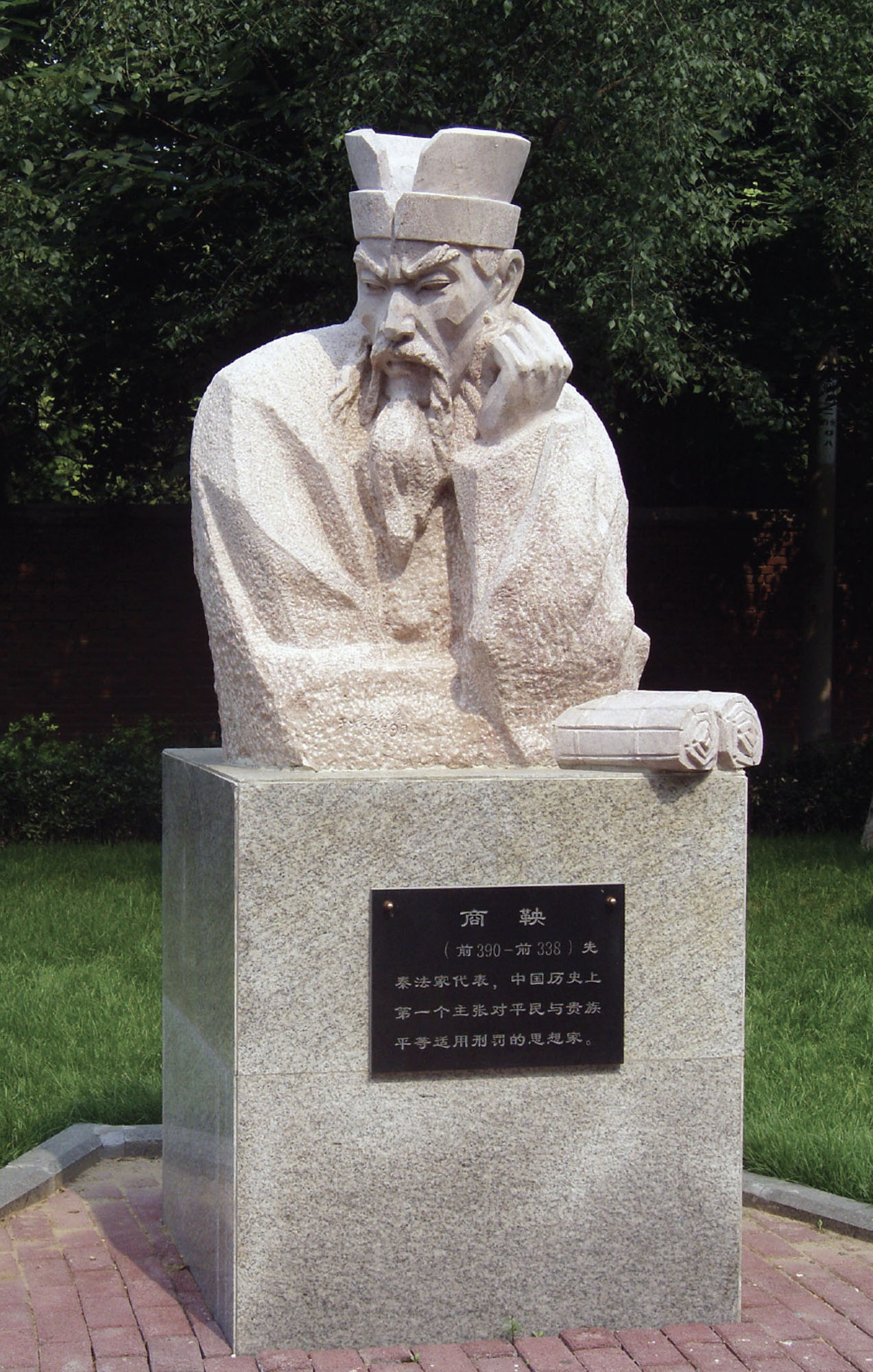 Statue of a man’s upper body. He is looking down and holding two scrolls underneath his elbow.