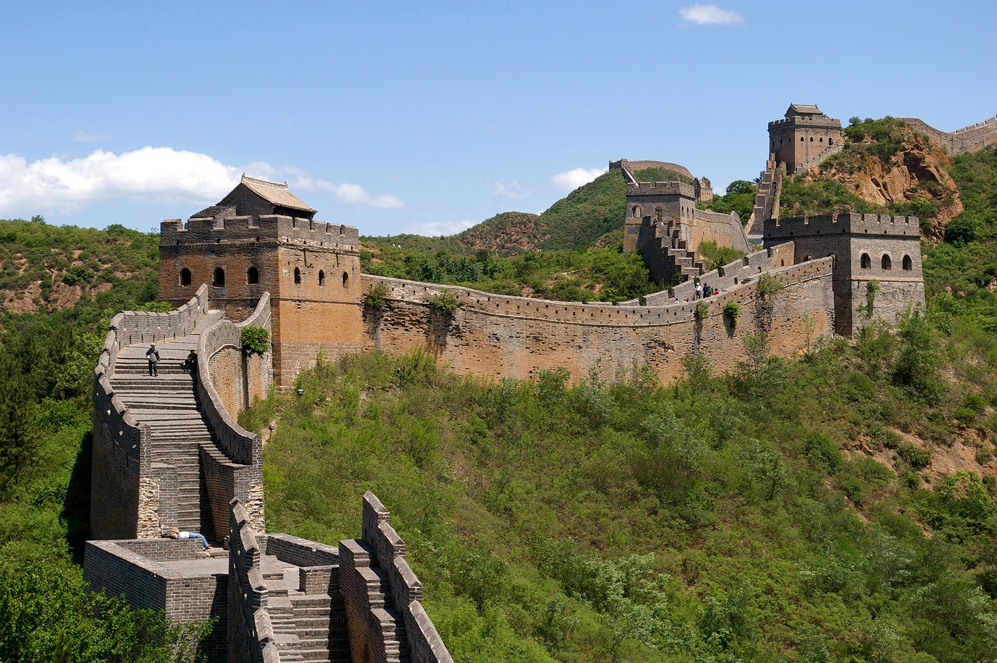 Panoramic view of the Great Wall of China. Ancient structure of stairs, walls, and towers stretch across a mountain ridge and continues off into the distance. 