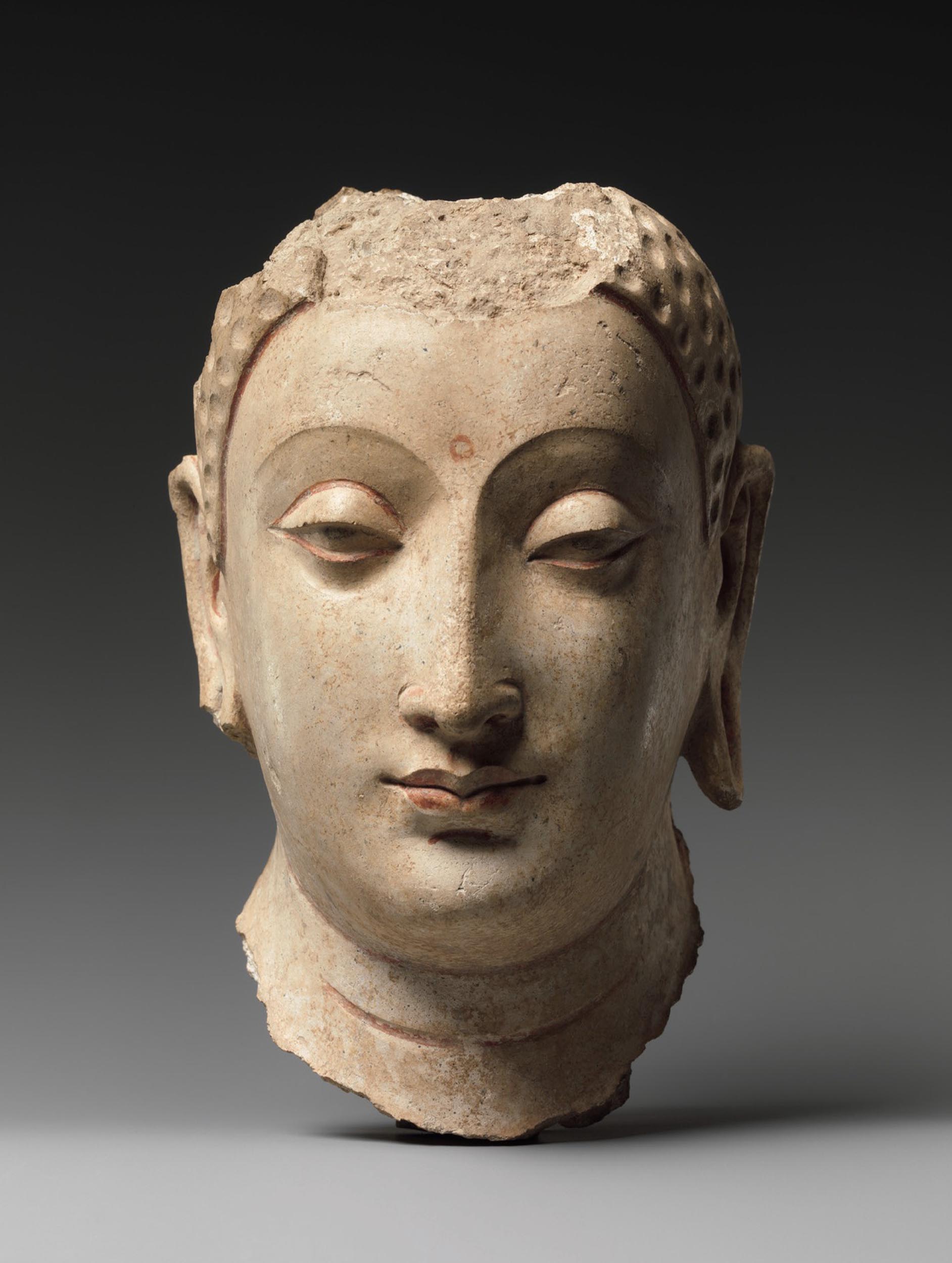 A light colored, broken and fragmented stone sculpture of Buddha’s head.