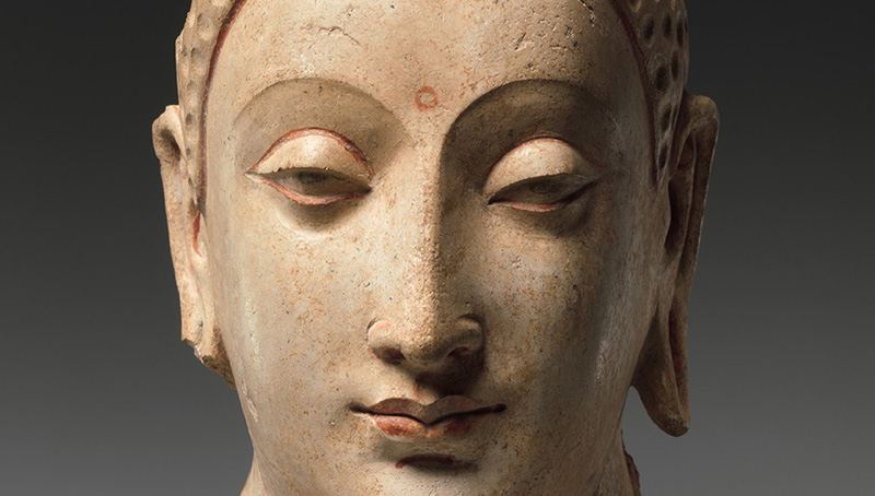 A light colored, broken and fragmented stone sculpture of Buddha’s head.
