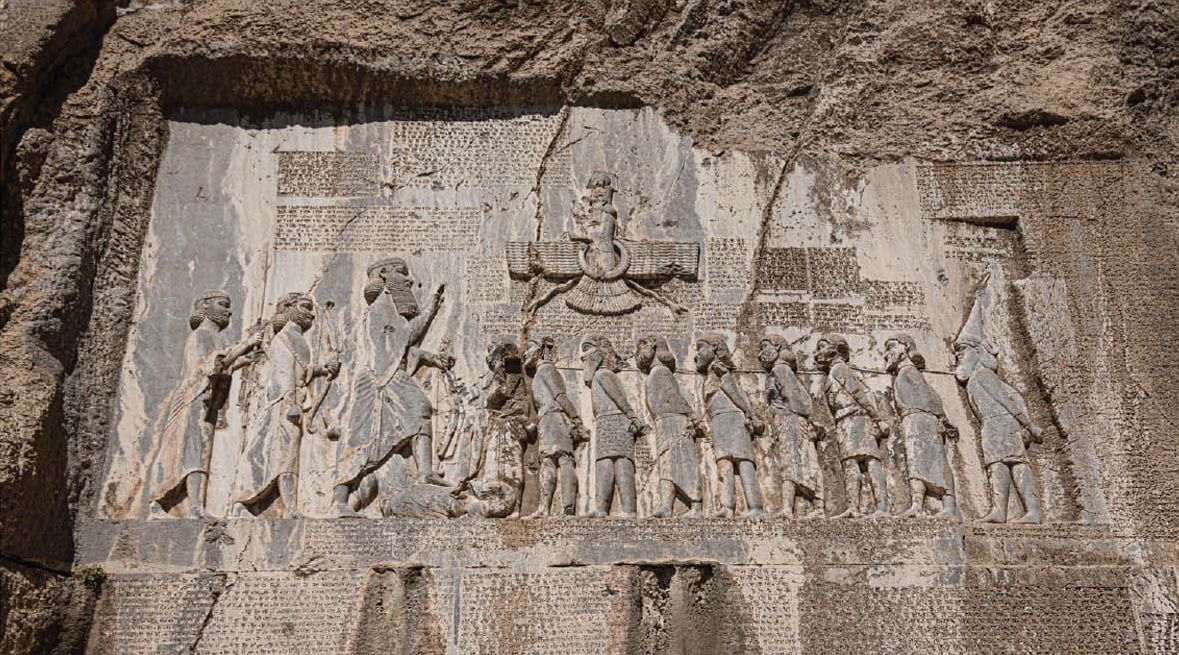 A stone carving depicting war scenes and the “Behistun Inscription”. It tells about the conquests of Darius the Great and shows him speaking to people he defeated. The inscription is written in three different languages.