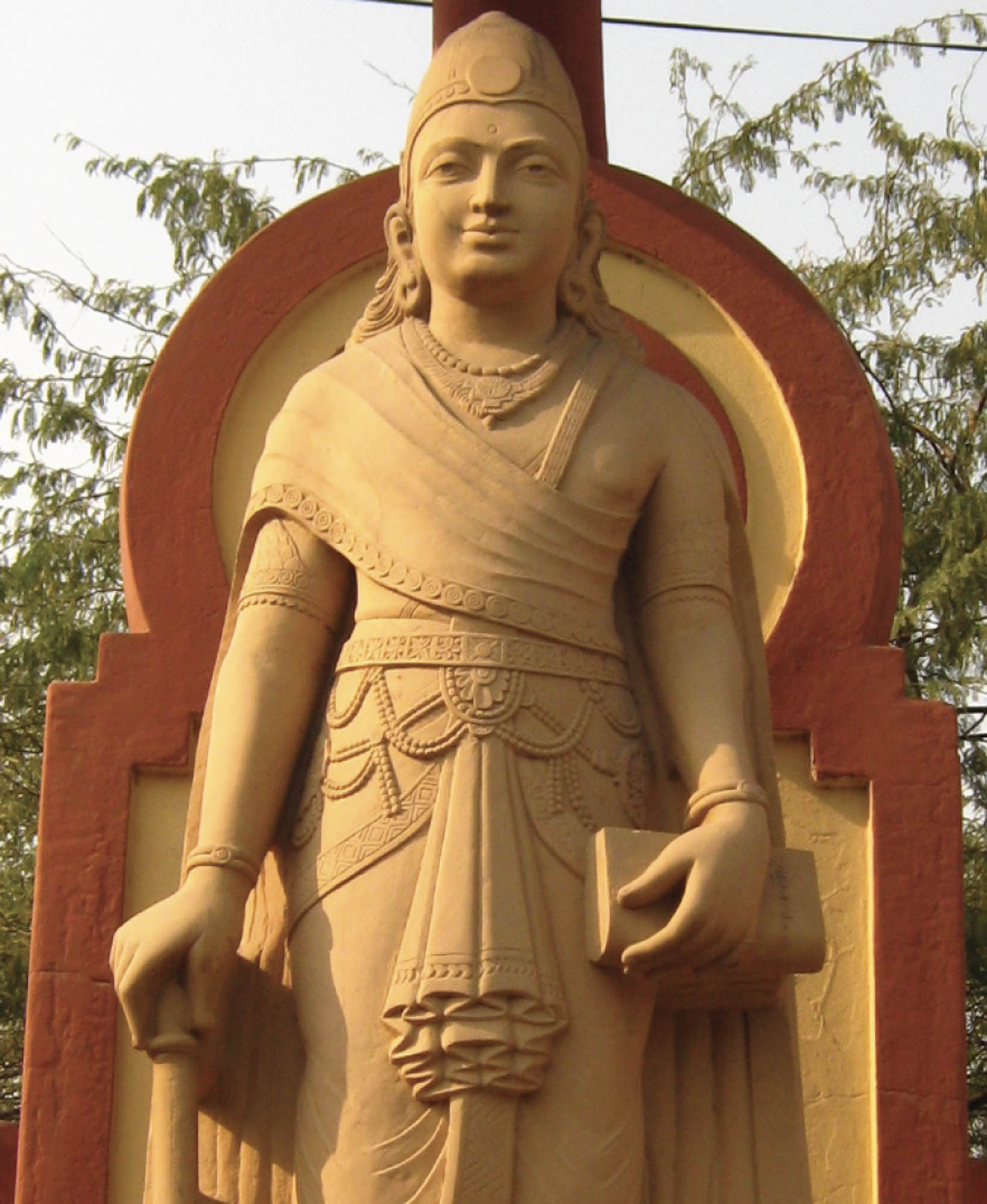 A sculpture of the Mauryan emperor Chandragupta Maurya. He is holding a book in one hand and wears a faint smile.