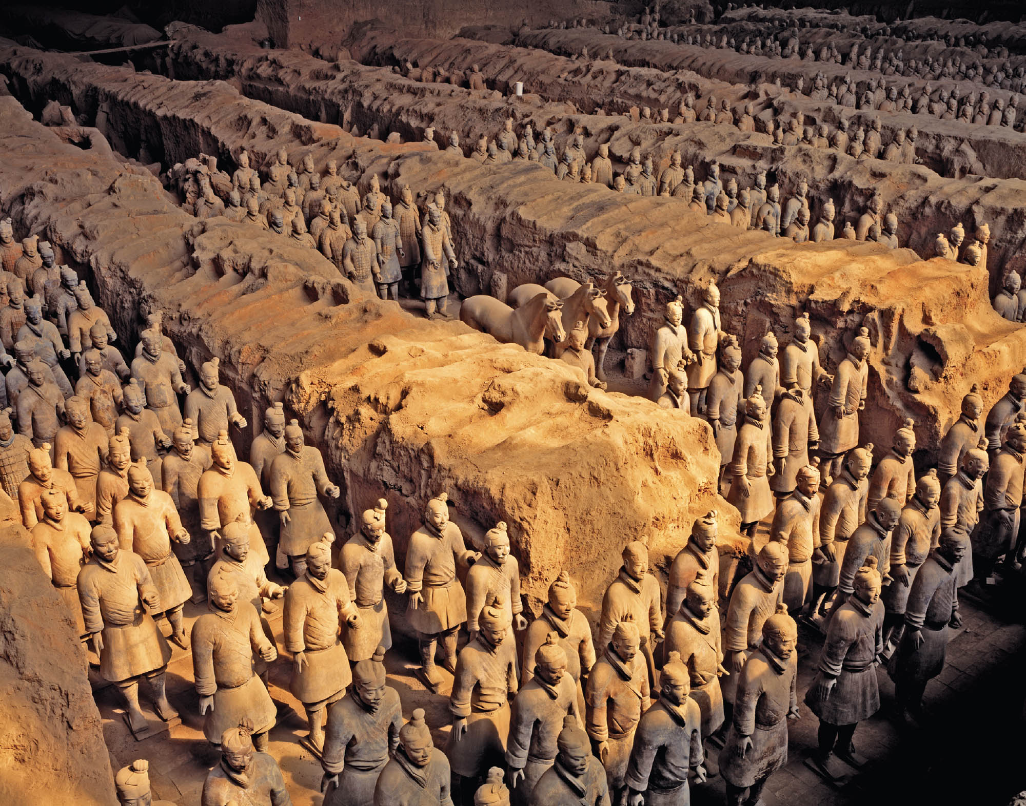 A picture of a vast number of terracotta warriors in various stages of ruin. The warriors are incredibly detailed and impressive sculptures. There are three horses in the center.
