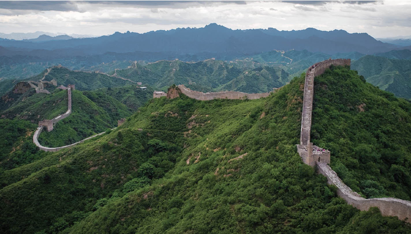 A birds-eye photo of the Great Wall of China shows the vastness of the wall against a green hillside
