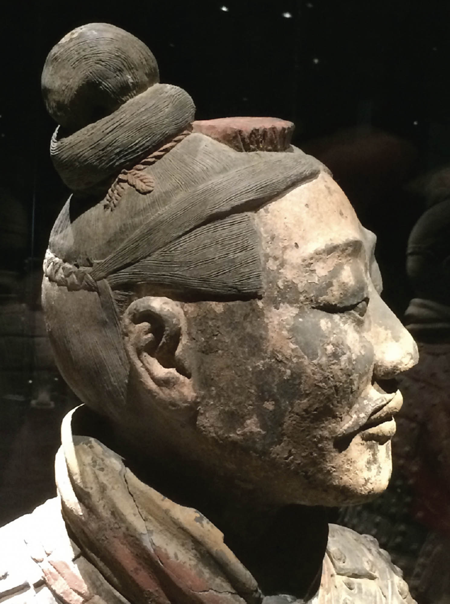 Close up of the head of a terracotta warrior shows the detail of the sculpture. The warrior’s face is extremely lifelike, and he wears his hair in a neat bun.