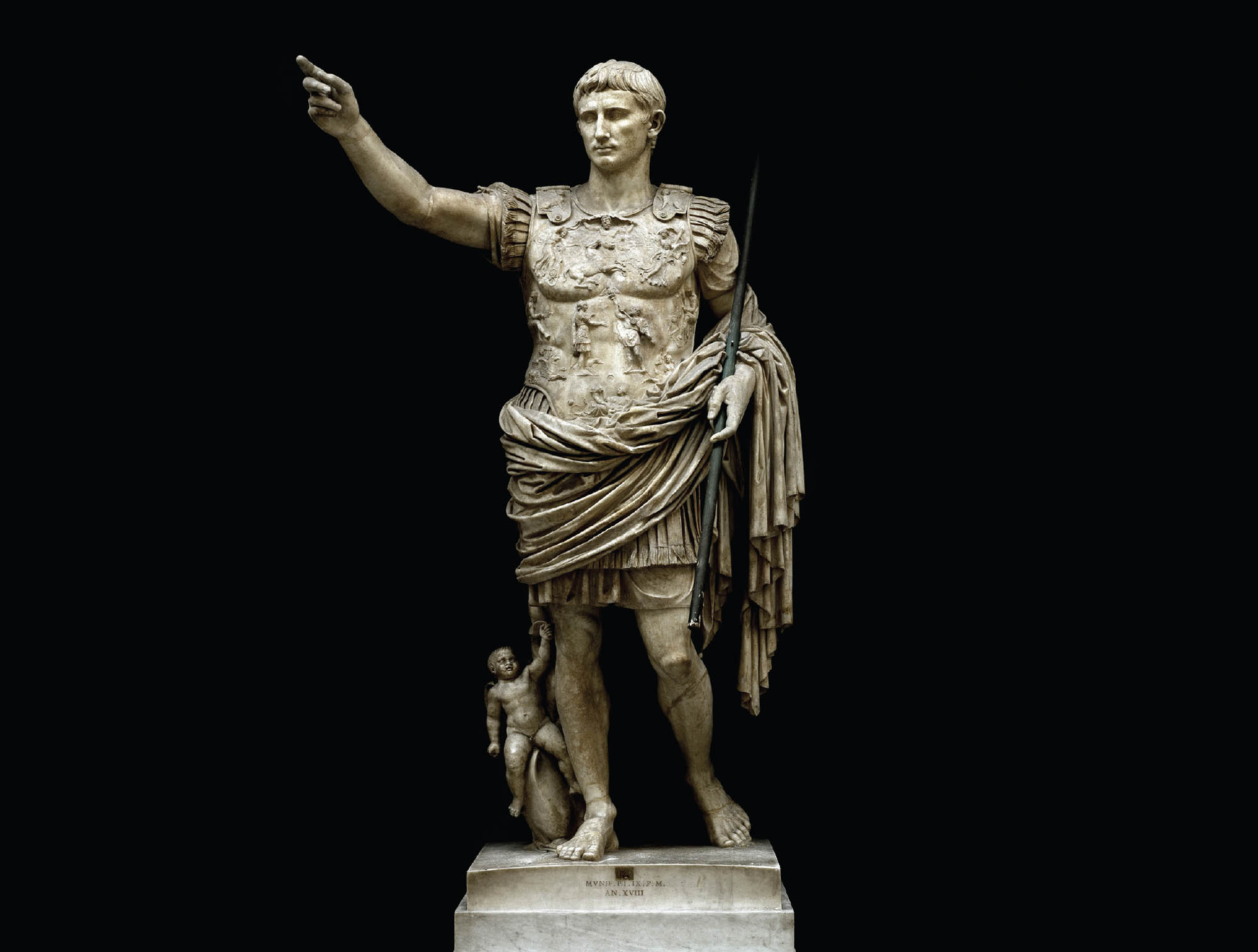 Marble sculpture of an emperor. He is wearing a shield embossed with detailed figures. A baby is at his side.