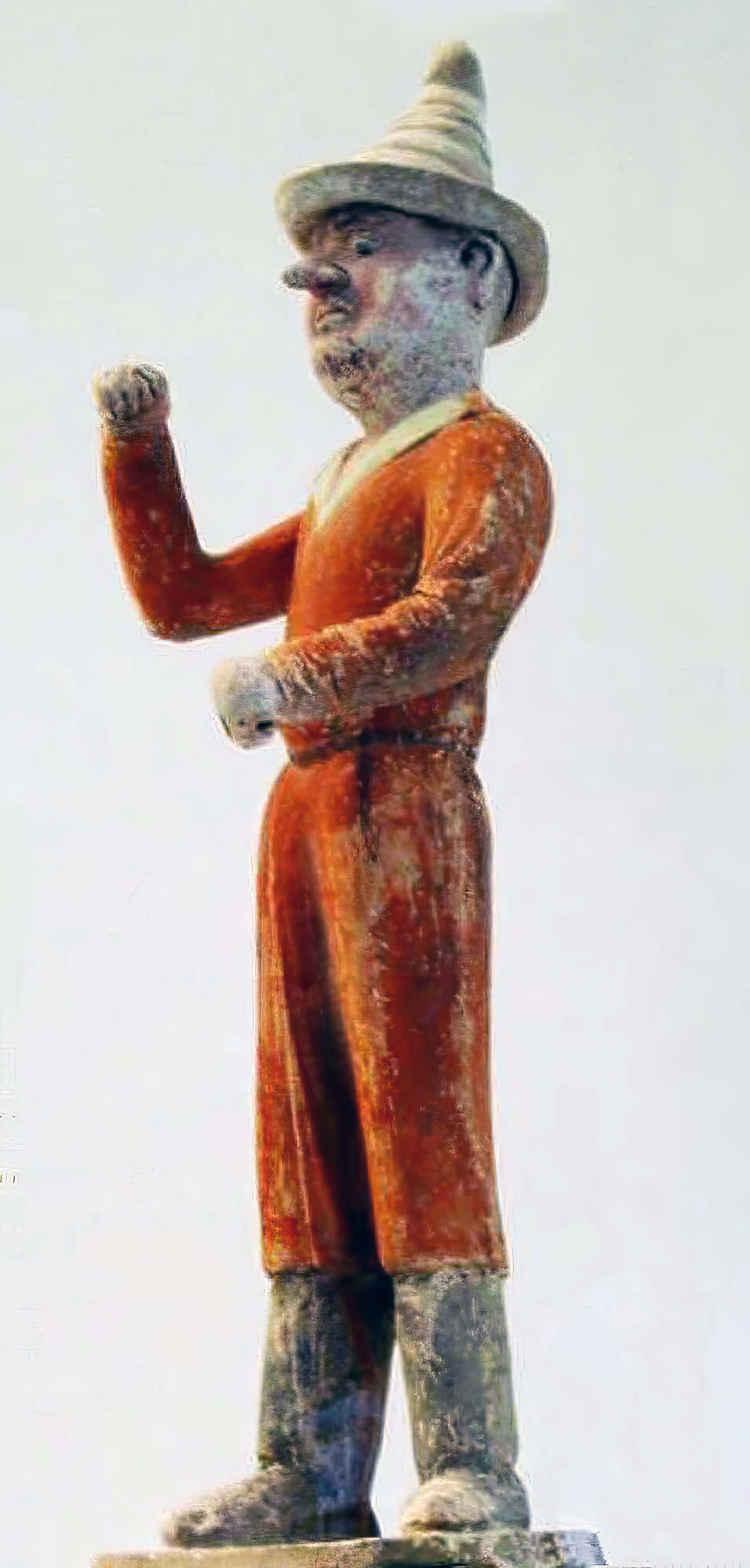 Photo of a figurine. The small sculpture is of a foreign merchant, wearing orange robes and a hat.