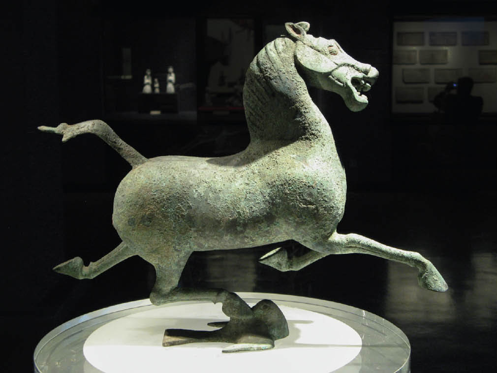 A sculpture of a horse. It is standing, balanced on one hoof, on the back of a bird.