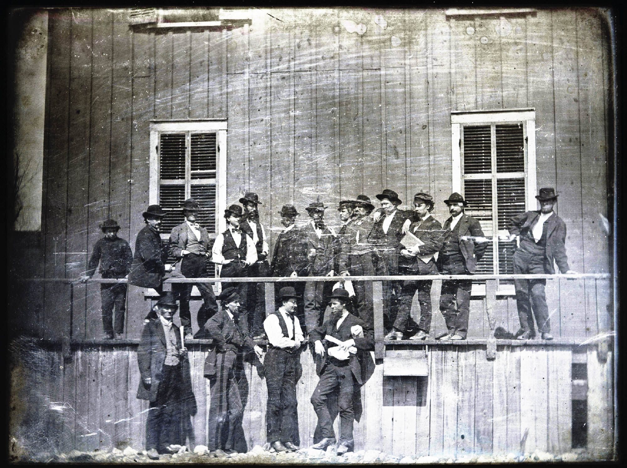 A group of men, dressed in suits, waiting outside of a wooden building