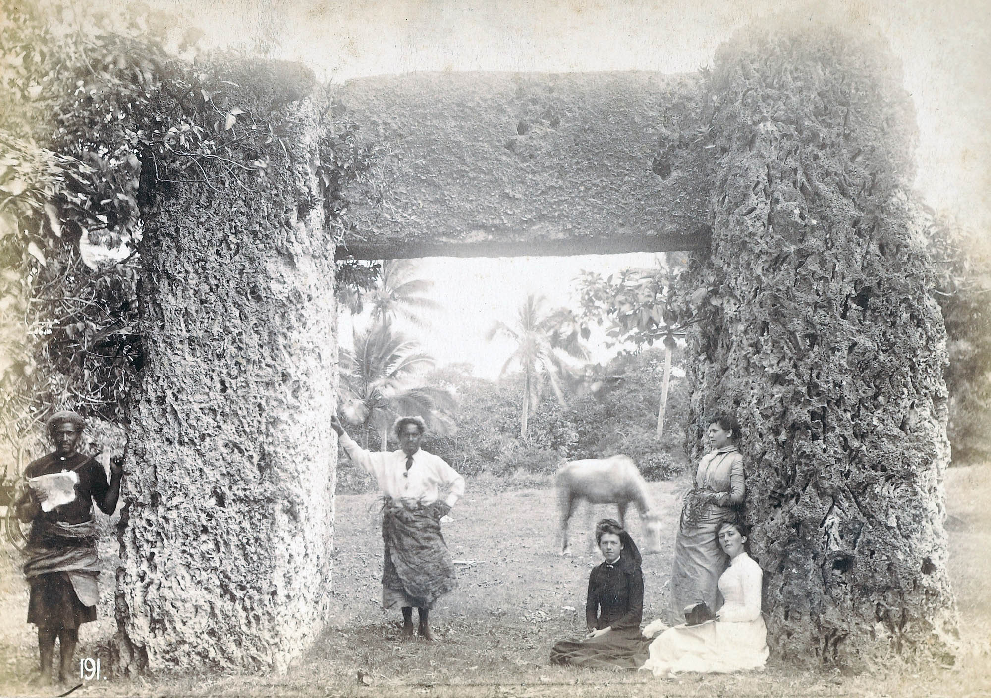A small group of five people stand underneath and beside a large stone gateway.