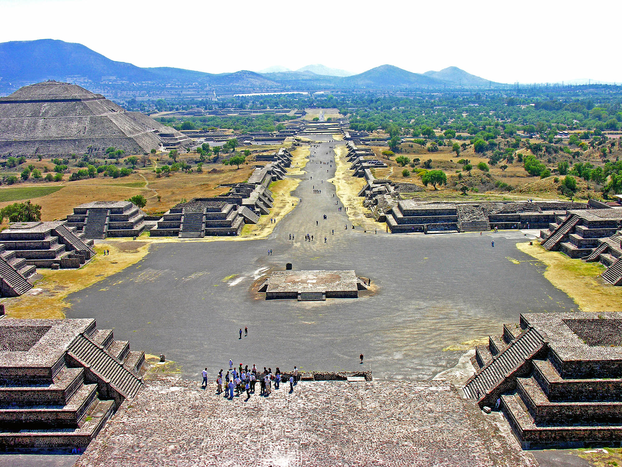 Birds-eye view of Teotihuacan showcasing the road that runs through the city, with many impressive pyramid-like structures surrounding.