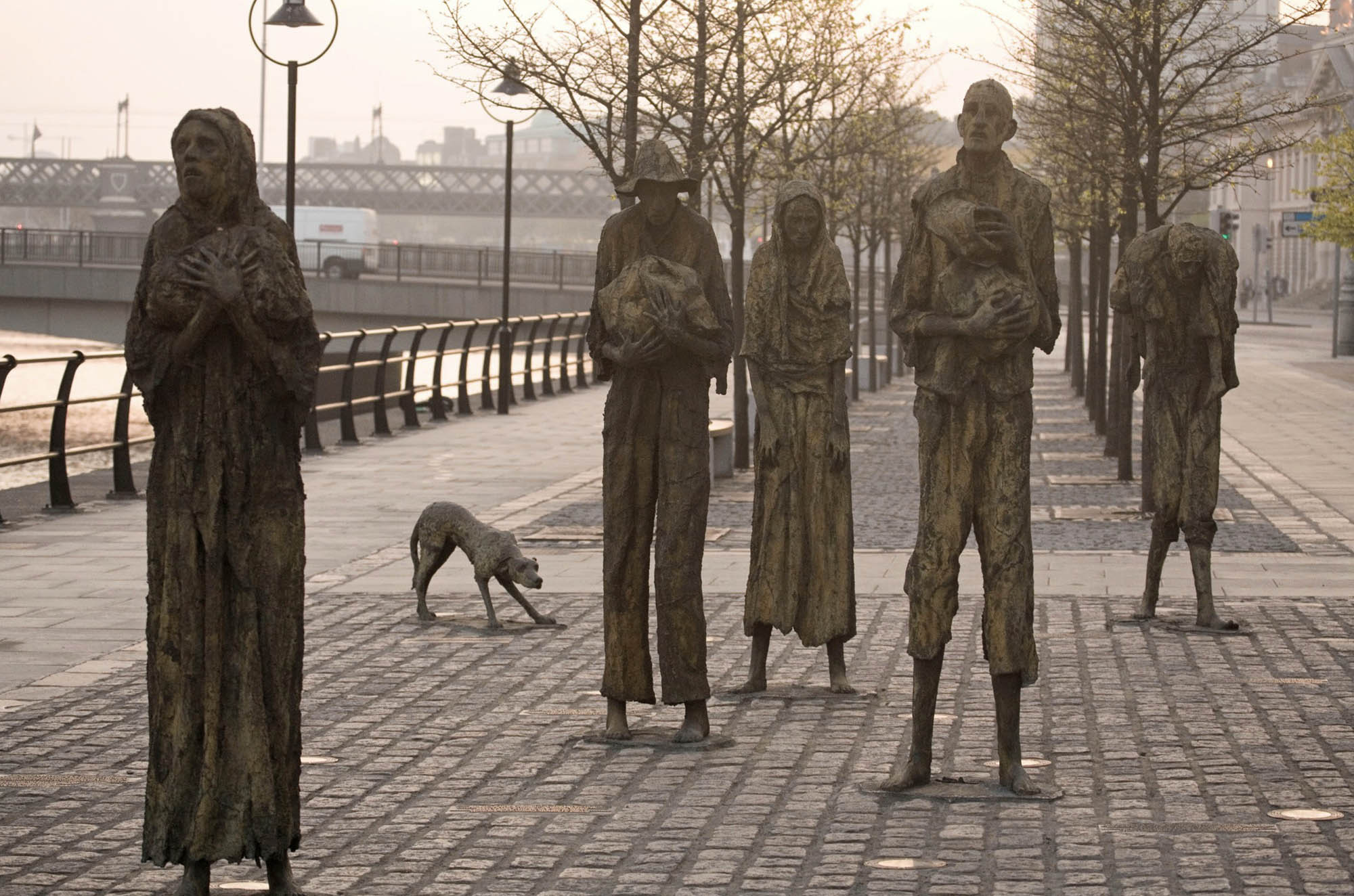 Photo of the Famine Memorial in Dublin, it features one dog and a group of five gaunt, life-sized bronze figures depicting various states of distress.