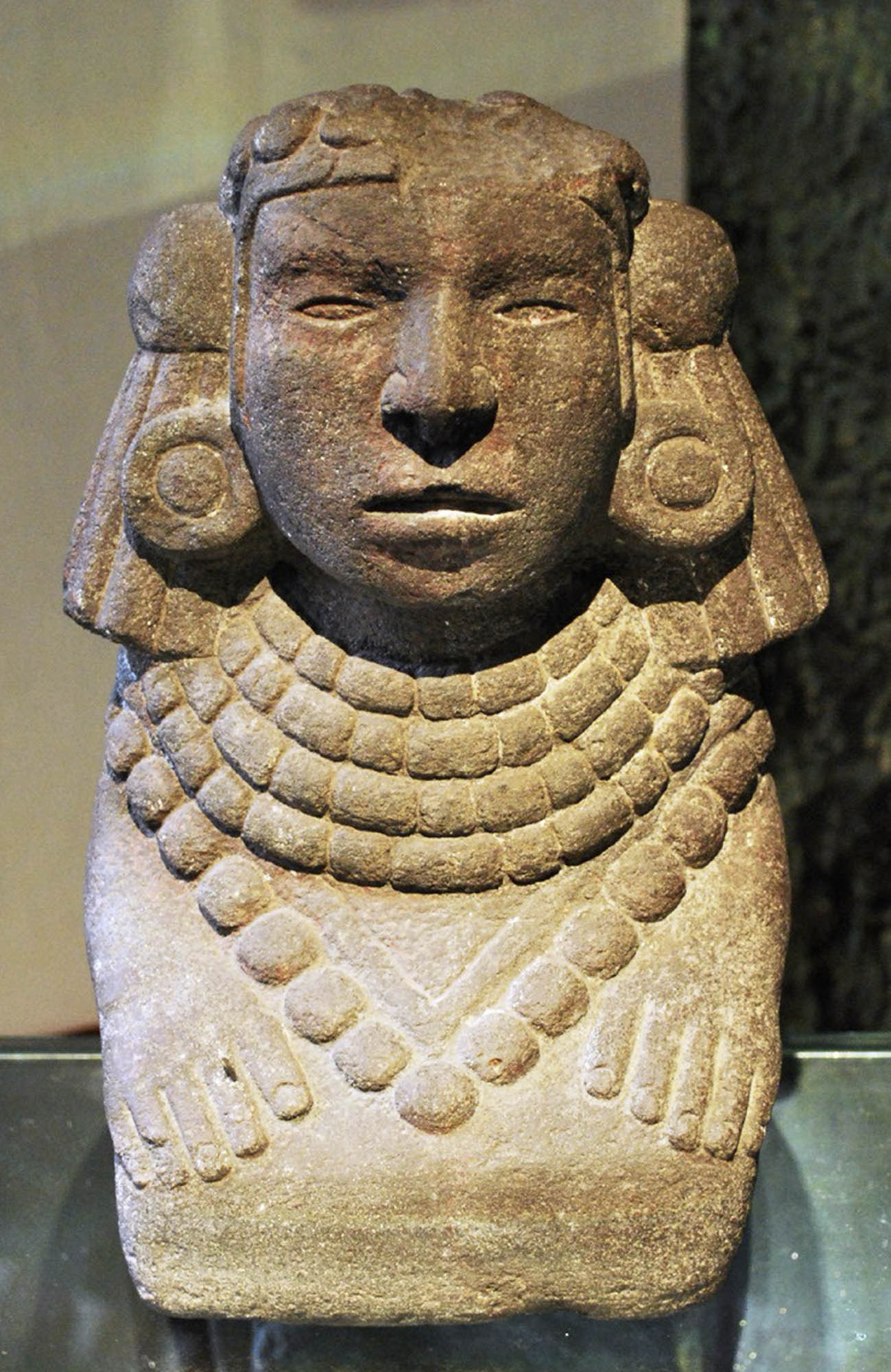 A stone sculpture of Tonantzin, depicting her with a serene expression and adorned with a layered necklace and headdress.