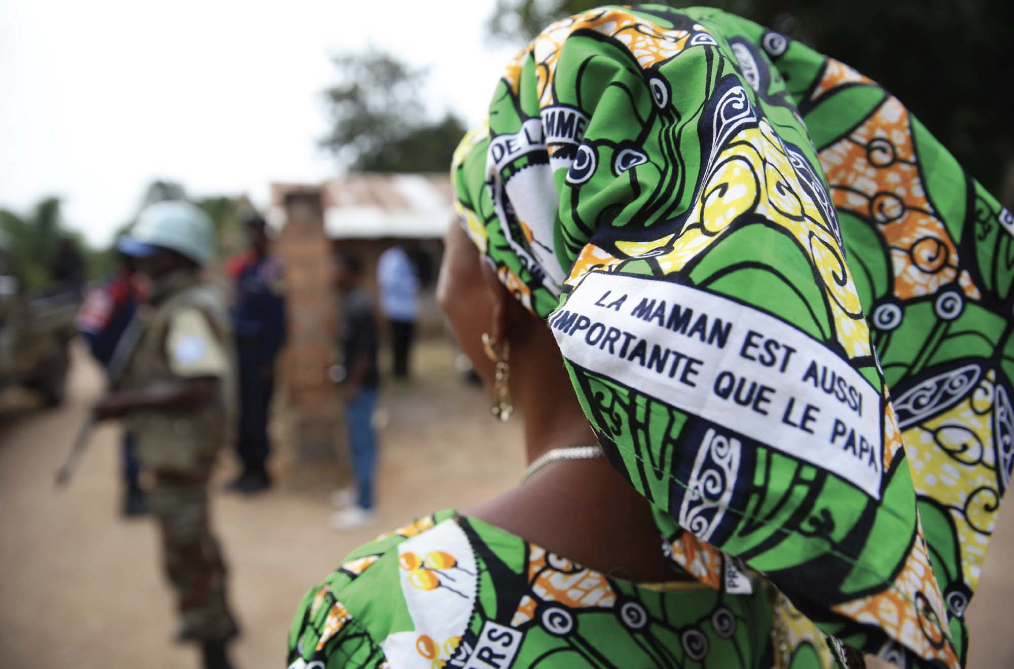 A photo of a Congolese woman wearing a head wrap with a slogan that translates to “Mom is as important as dad”