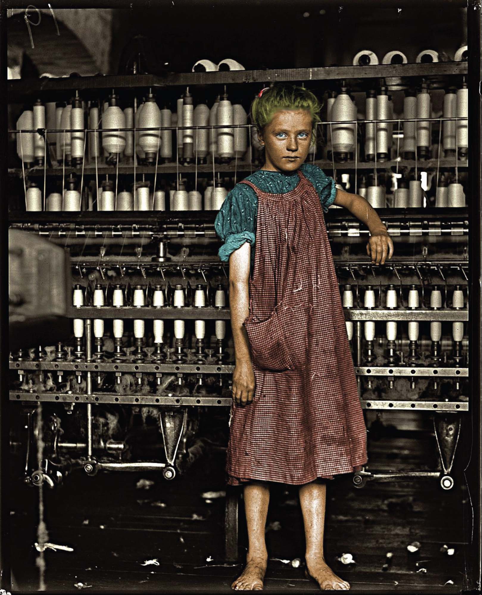 A young girl, wearing ragged clothing and without shoes, standing in front of a spinning machine at an industrial textile factory.