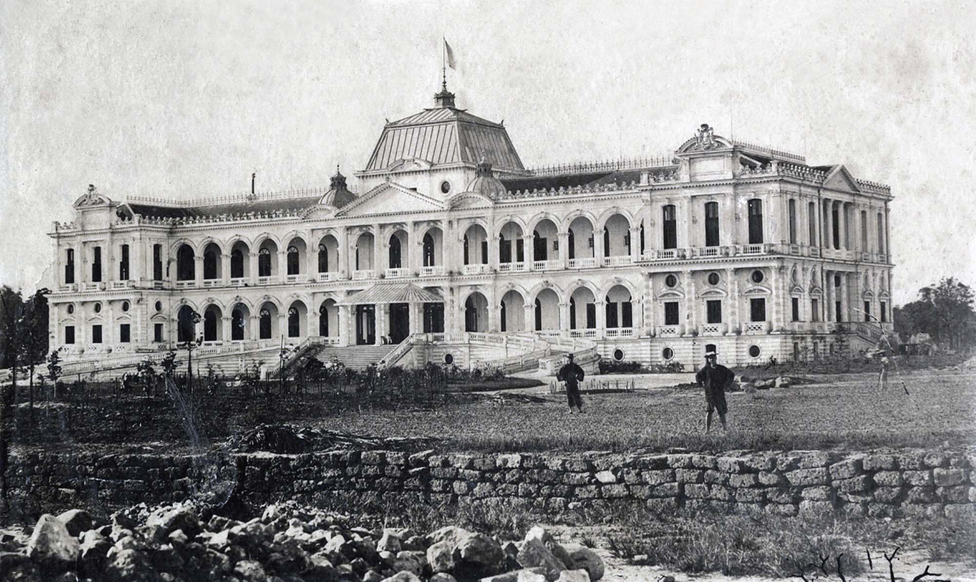 A photograph of a grand palace. The building is mostly rectangular, with two levels and many arched windows. There is a large staircase leading up to the palace and a stone wall before it.