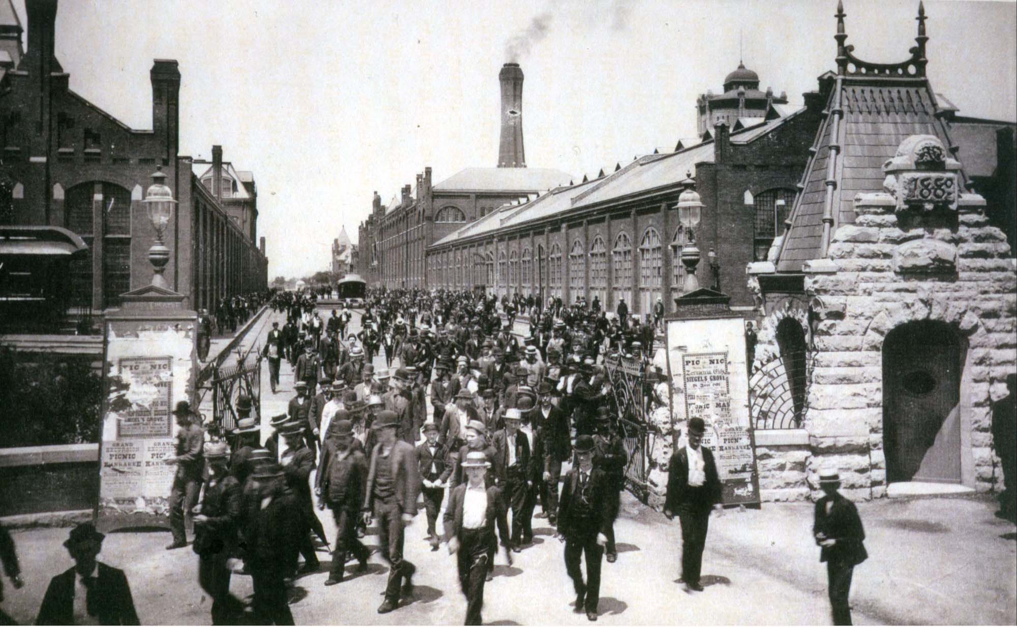 A photograph of a large crowd of working-class individuals. Many of them have dirt on their faces and are wearing ragged clothing. Some are children.
