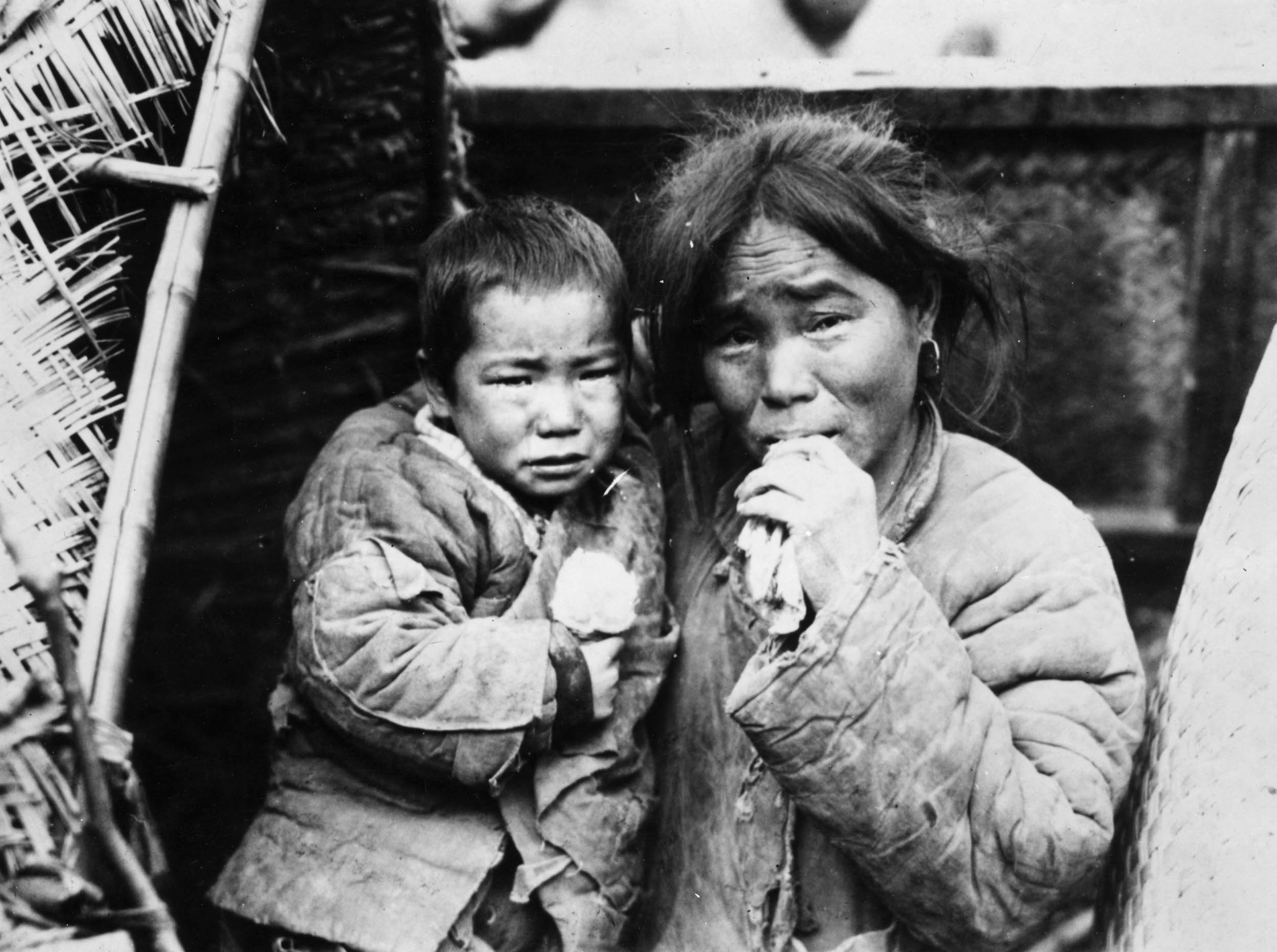 Black-and-white photo of a distressed woman holding a young child, both in worn clothing, during a time of hardship in early 20th-century China.
