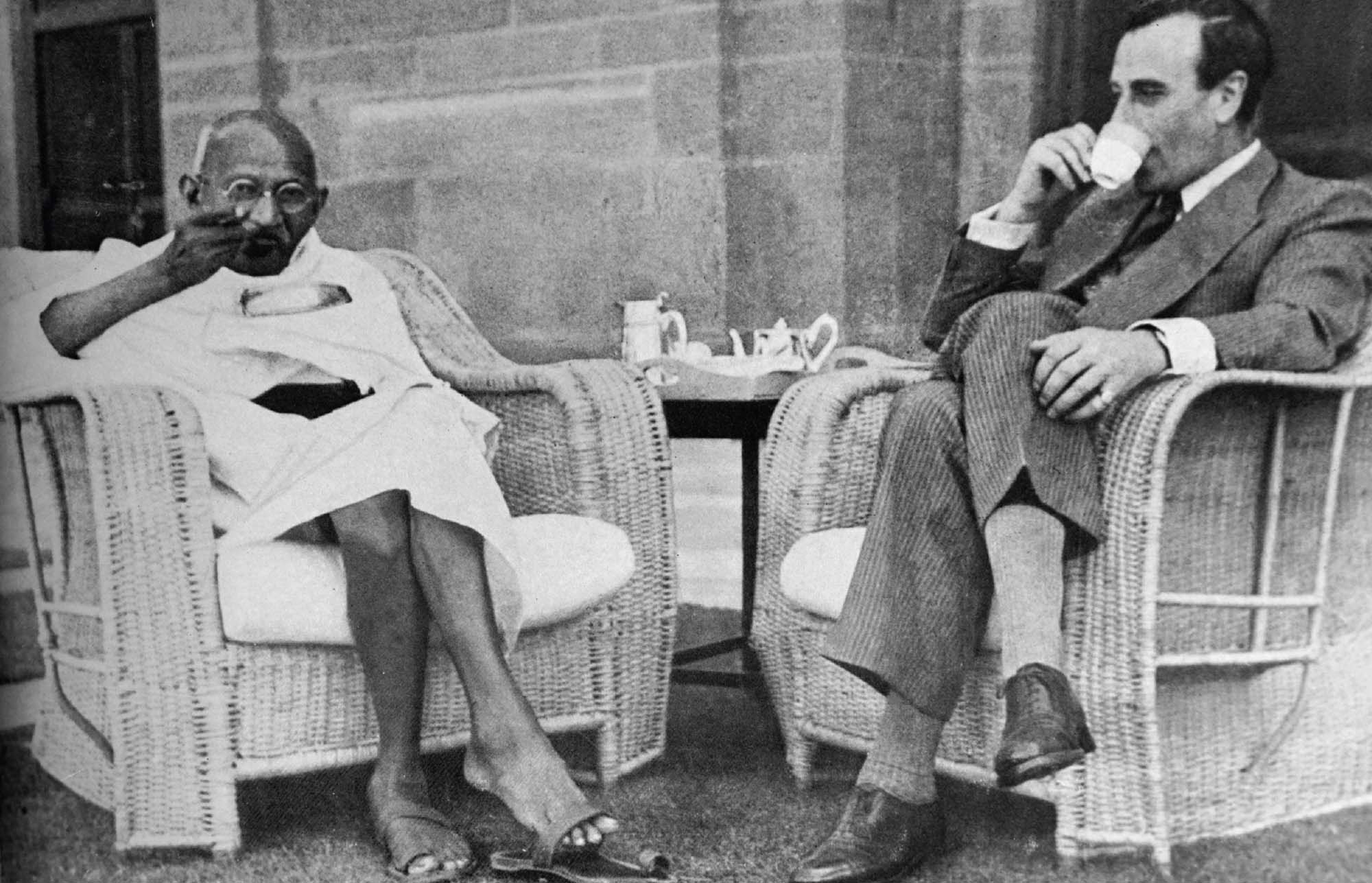 Gandhi and Lord Mountbatten drink tea while seated on wicker chairs outside.