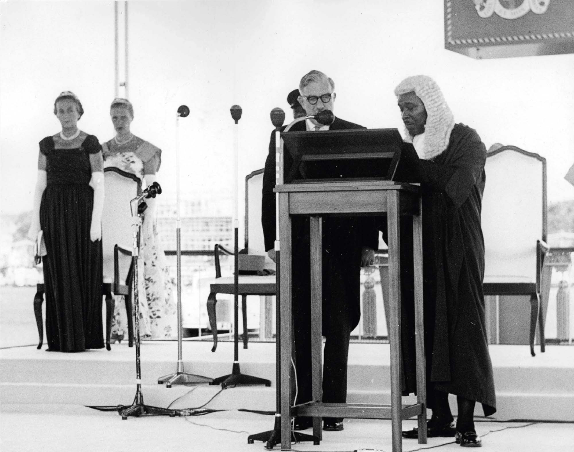 Two men, one in judicial robes and wig, stand at a lectern during a Nigerian Independence Day ceremony.