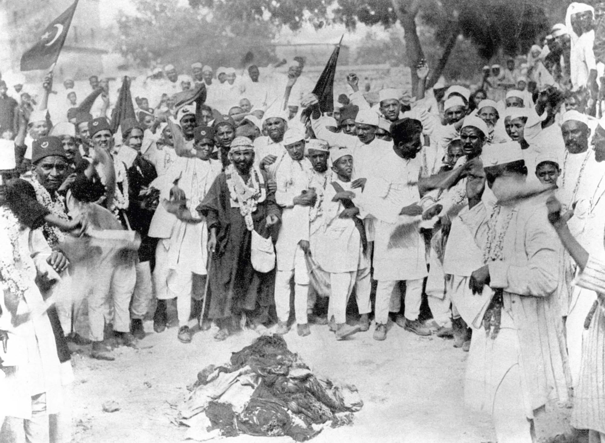 A boisterous crowd stands around a bonfire made from boycotted, imported British goods.