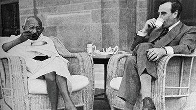 Gandhi and Lord Mountbatten drink tea while seated on wicker chairs outside.