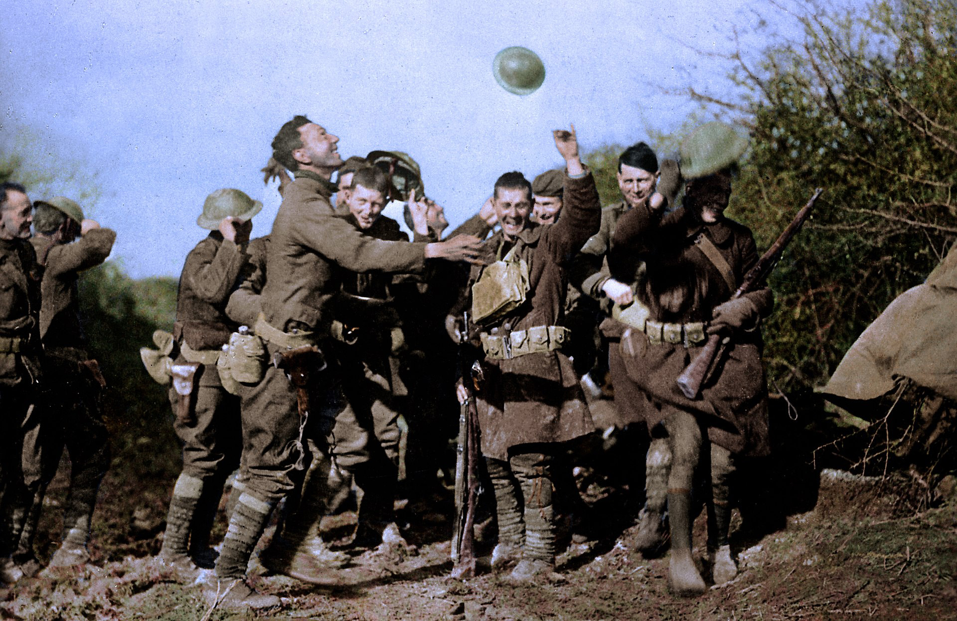 Smiling, celebrating soldiers cheer and toss helmets into the air at the news of the end of the First World War.
