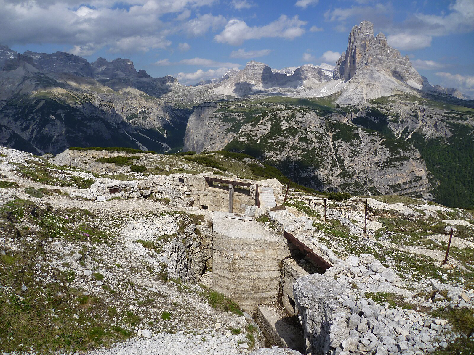 Trenches, tunnels, and emplacements located on top of a mountain. A larger mountain range is off in the distance.