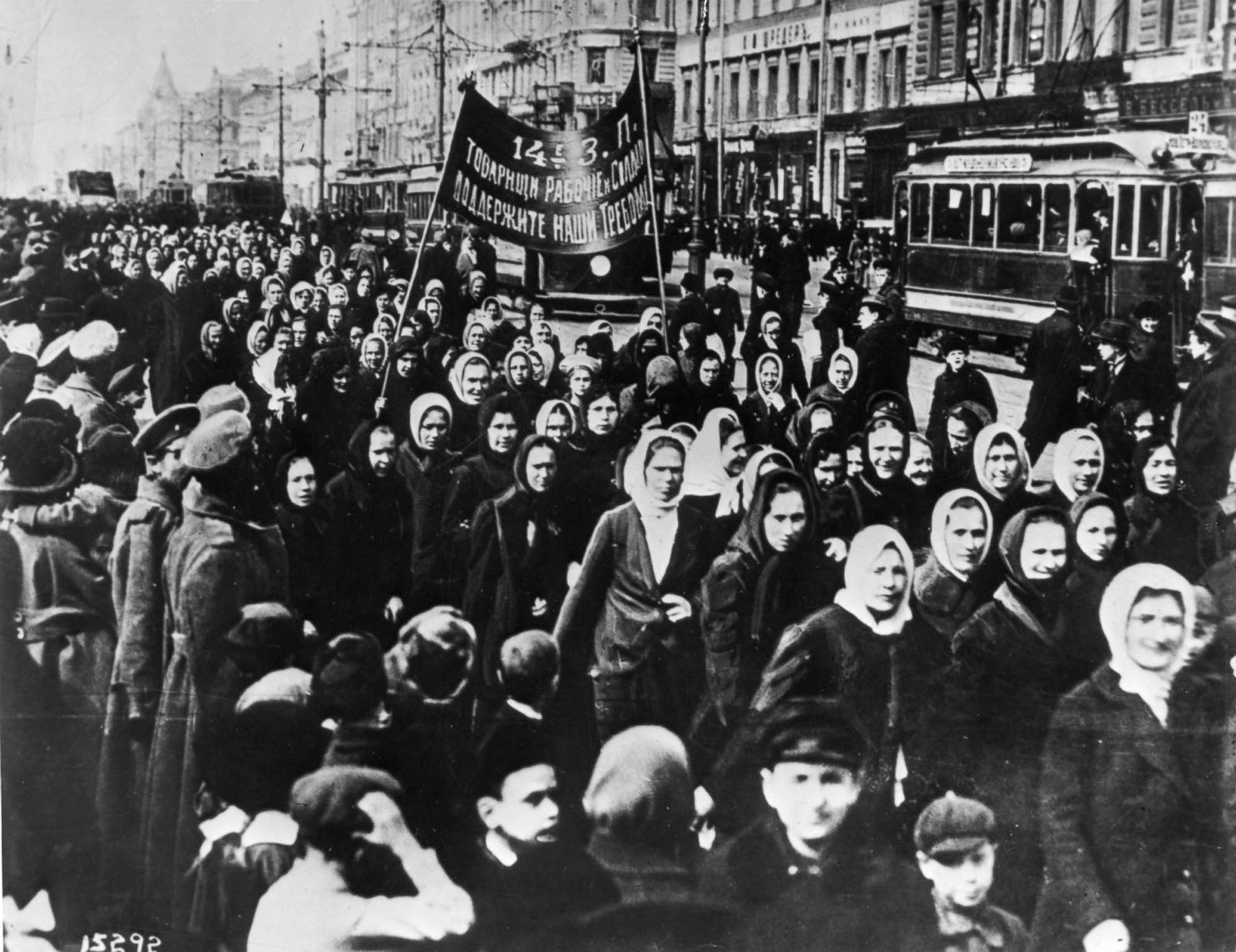 Photograph of many women marching down the street, holding up a banner.