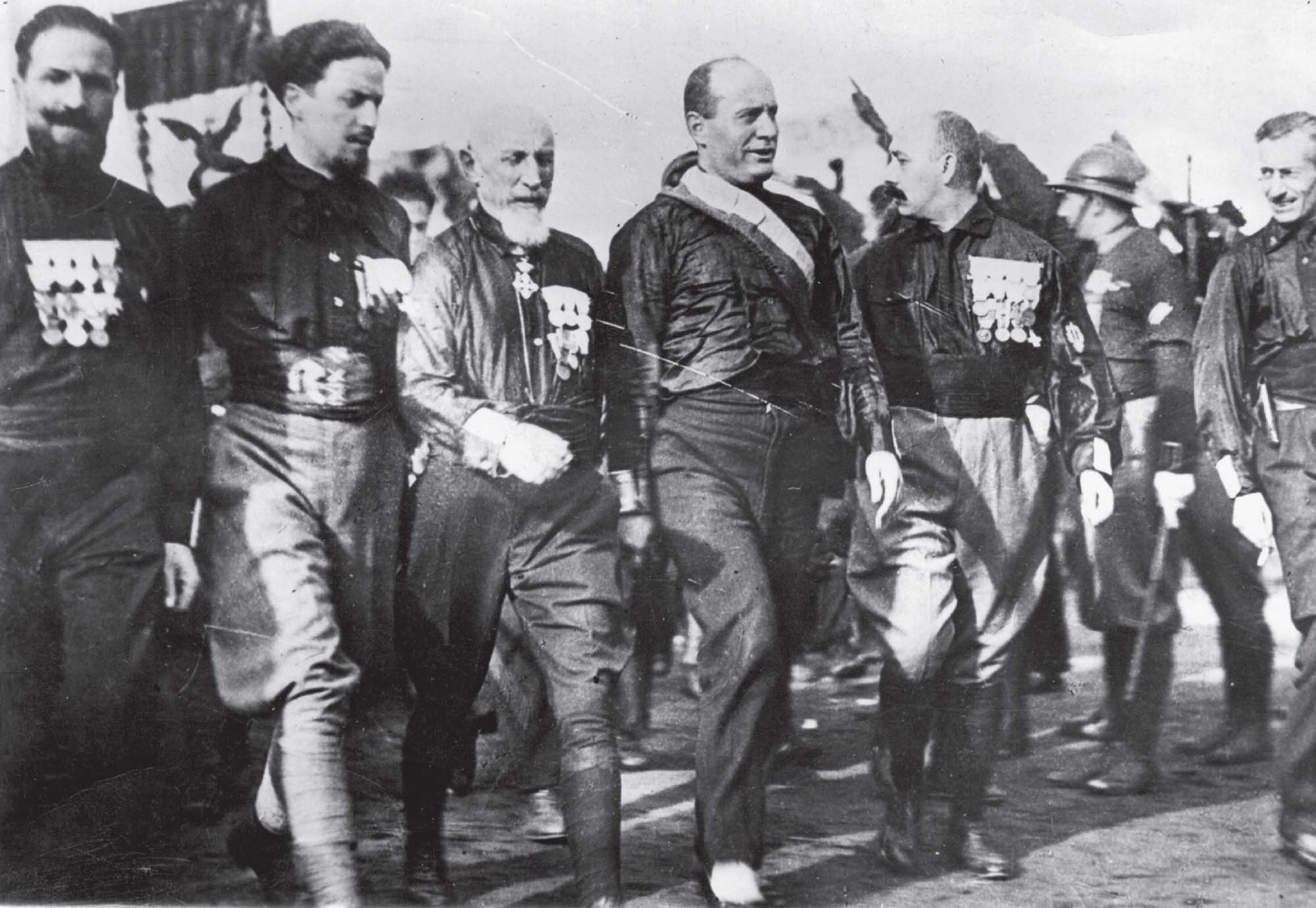 Photo of Italian dictator Benito Mussolini walking besides decorated members of the Italian military.