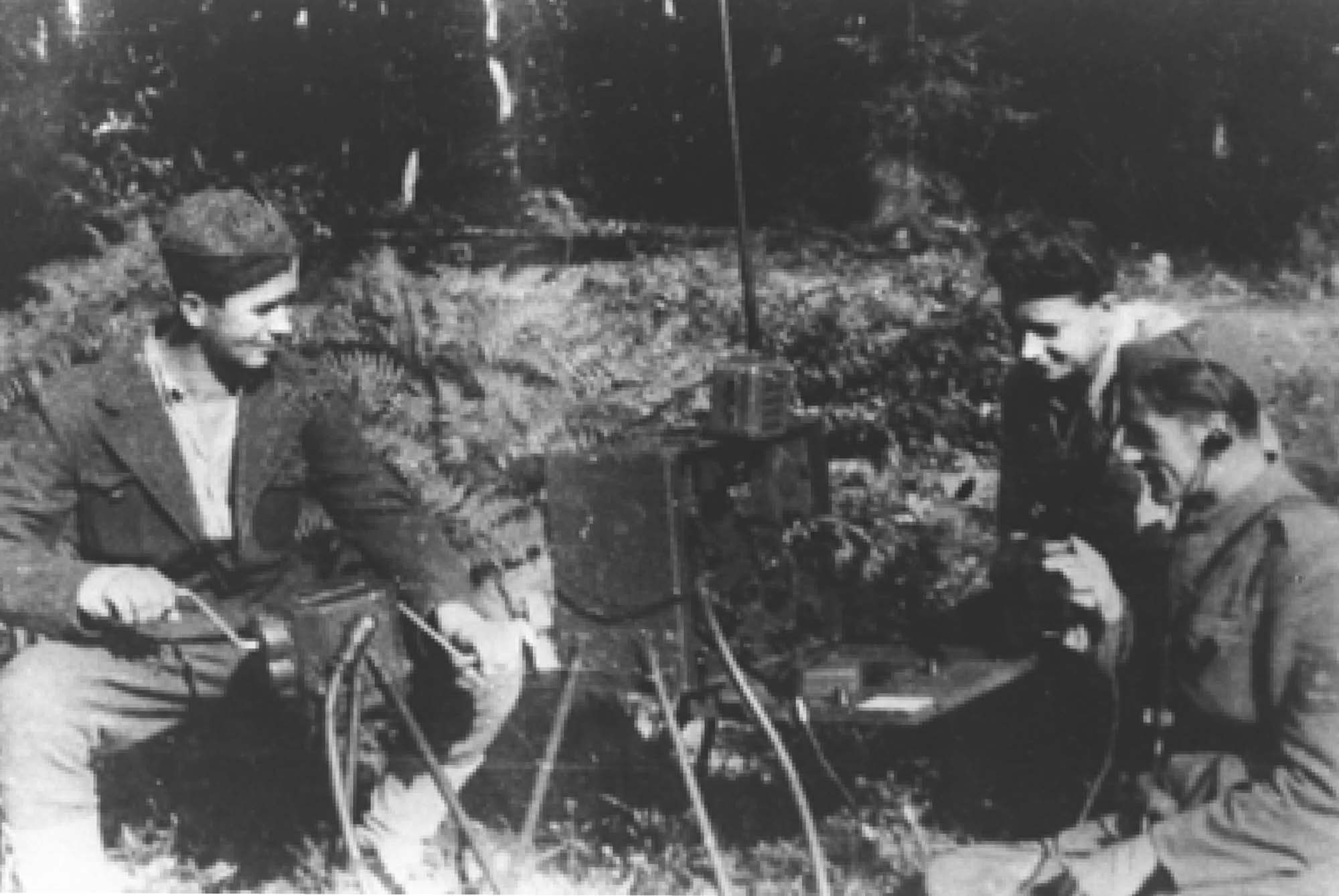 Photograph of three young man sitting around a radio.