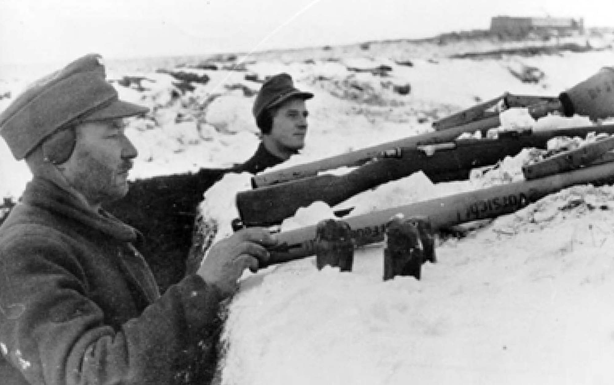 Photo of two soldiers, standing in a snowy trench operating weapons.