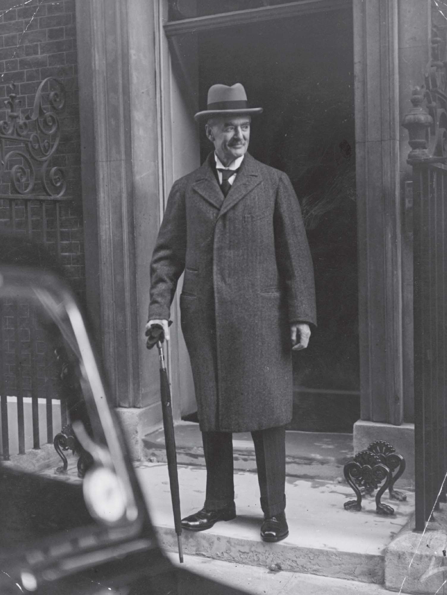 Black and white photo of a man in suit and hat holding an umbrella.