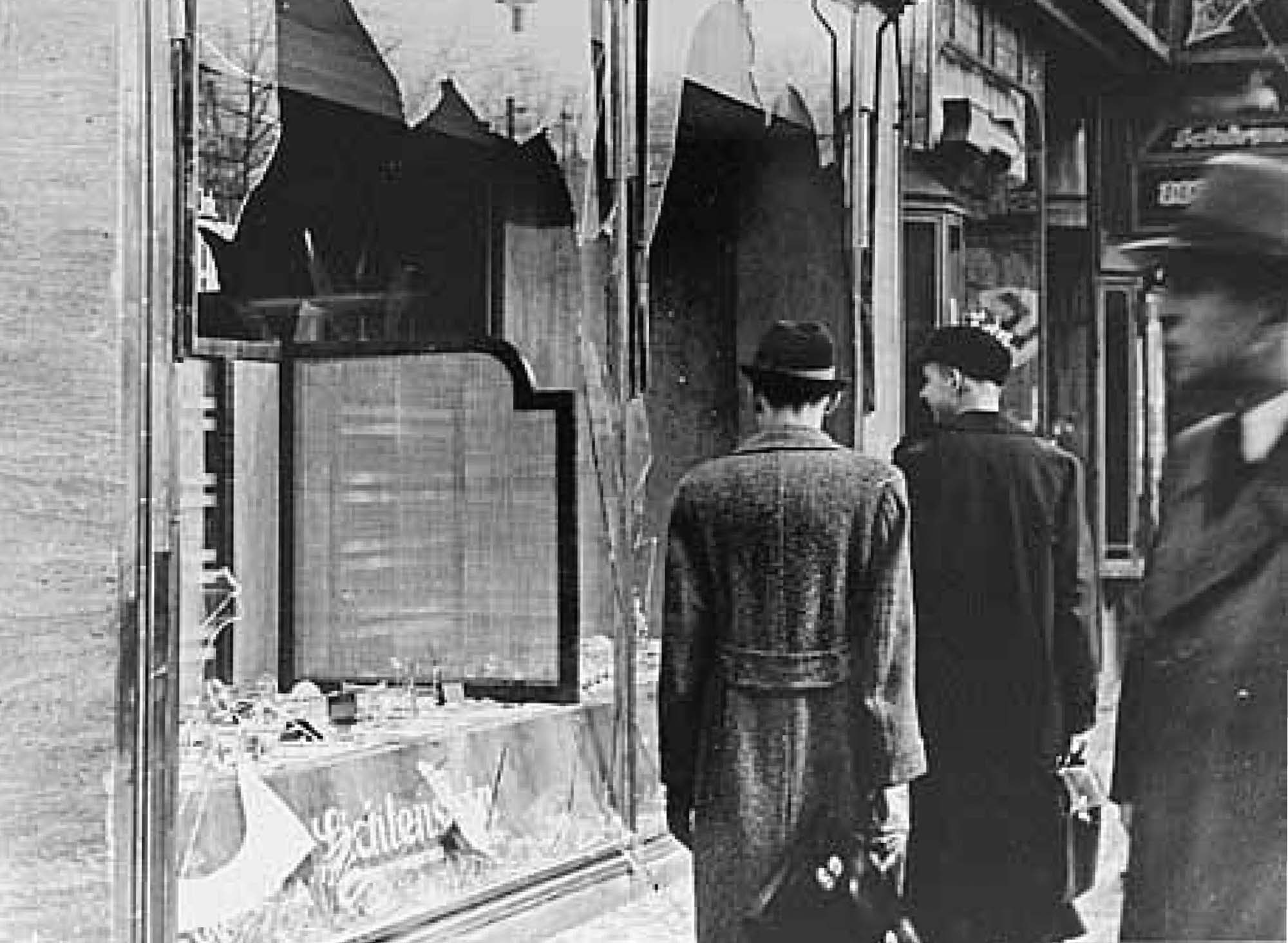 A photograph shows three men in suits and top hats standing in front of a storefront. The window of the storefront has been entirely broken.