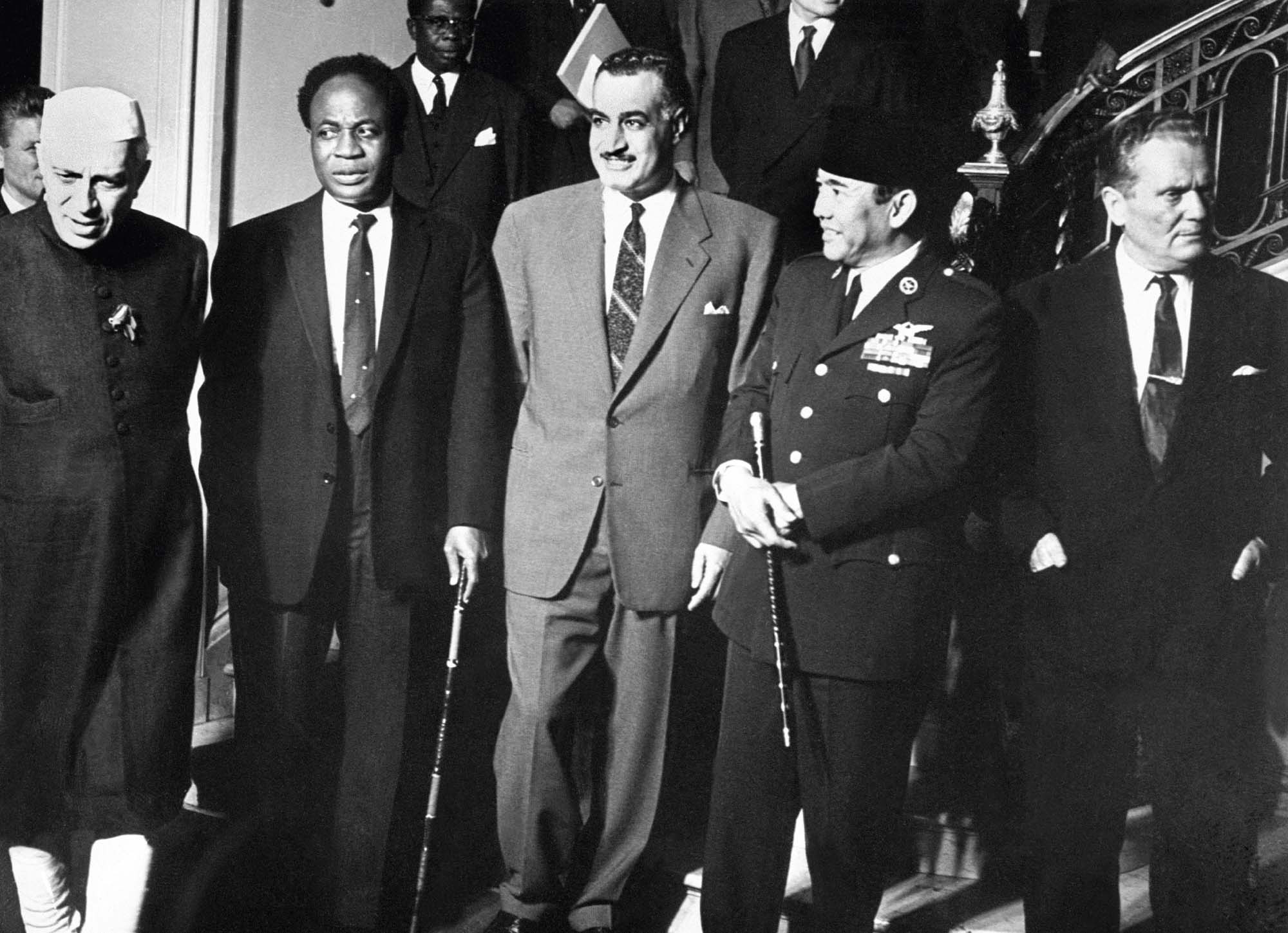 Five men stand together in front of a grand staircase.