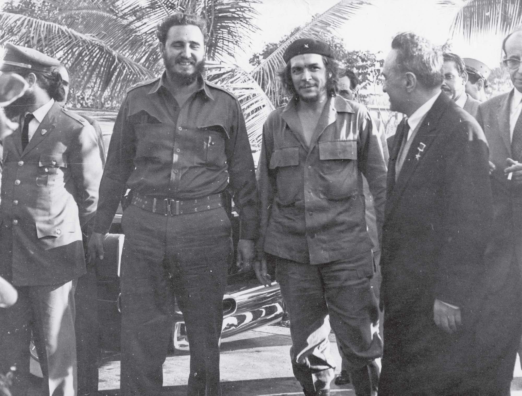 Several men are walking down the street together, smiling and in conversation. Two of the men are dressed in Cuban military gear, and the others are in suits and ties.