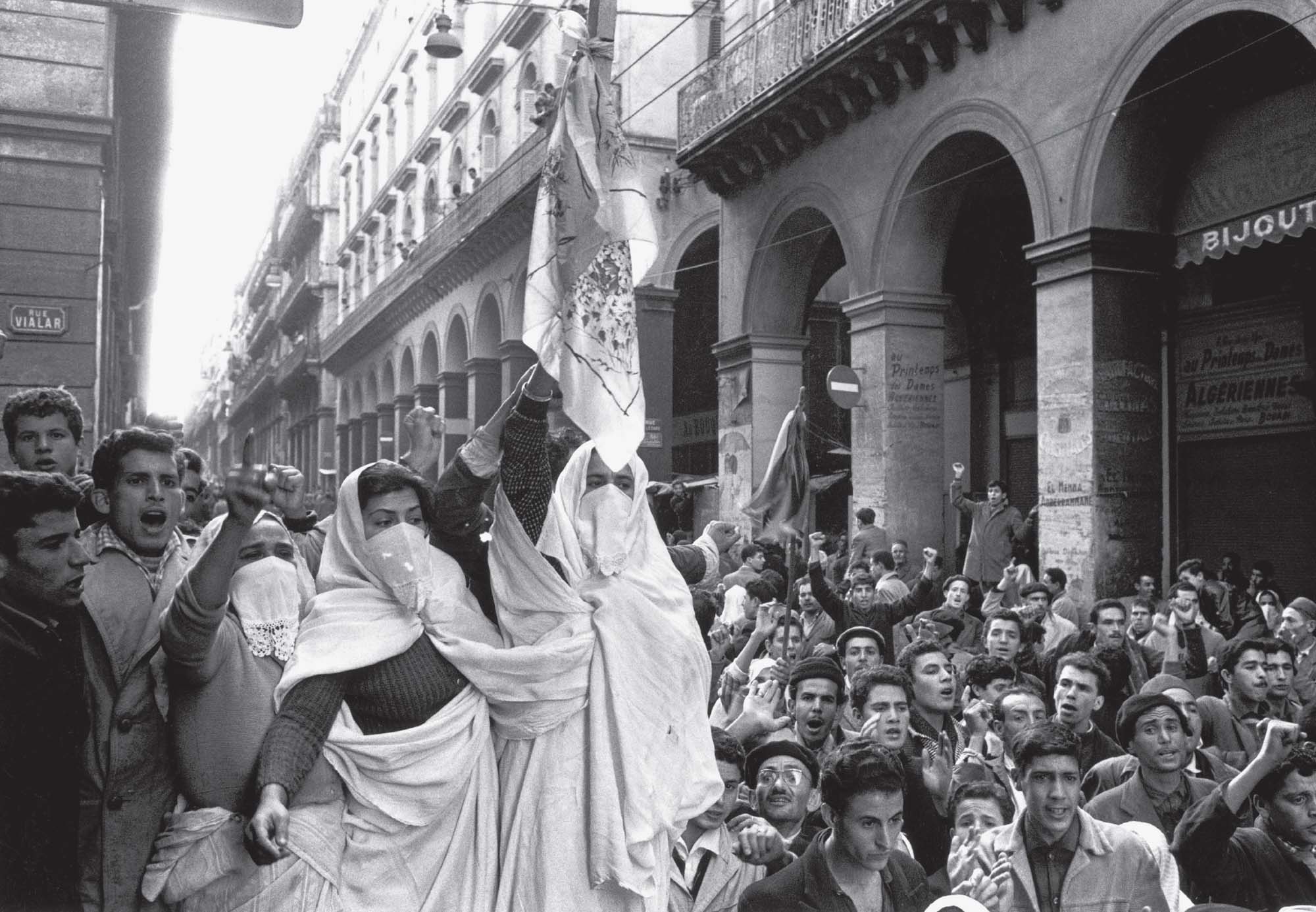 A crowd fills the street and carrying flags to protest the war in Algiers in 1960.