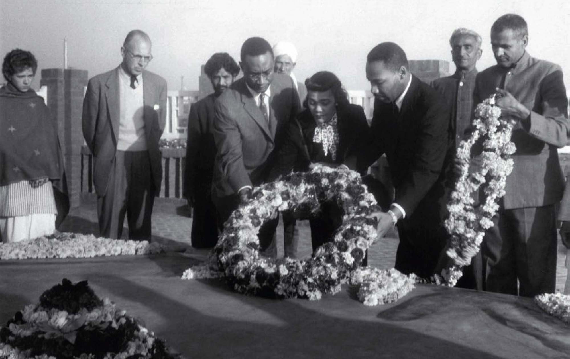 Black and white photo of several people laying down a flower wreath and garland on a stone memorial.