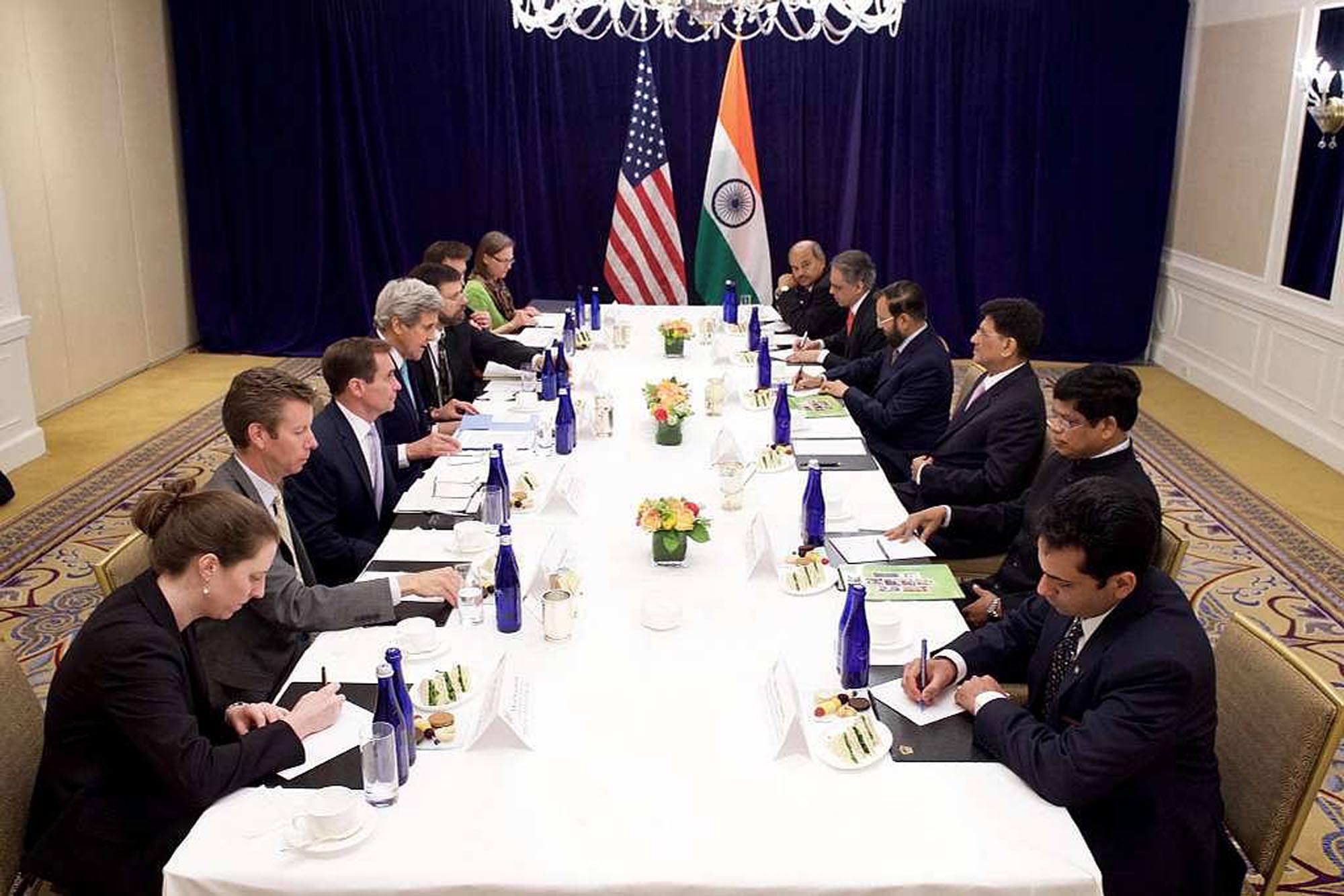Wide angle view of a large conference table with delegates from the USA and India sitting across from each other.