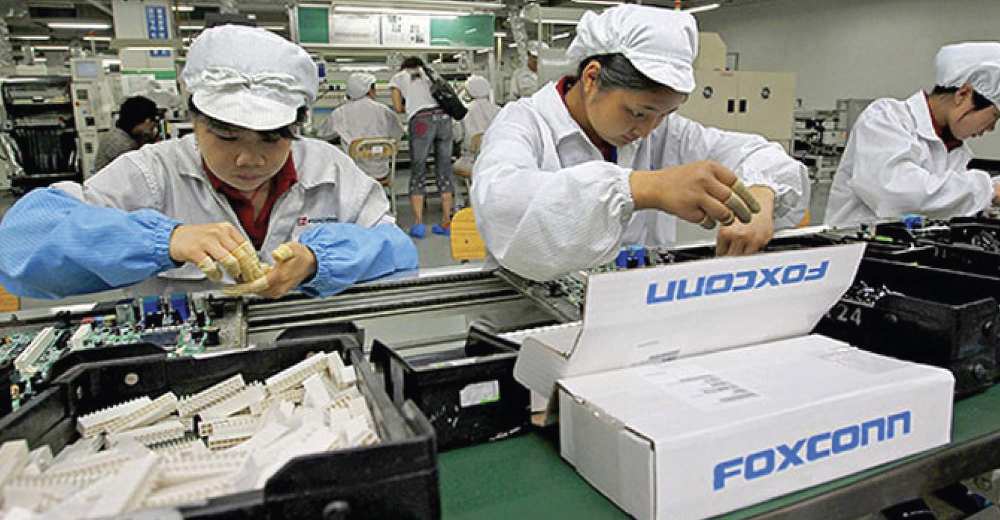 Modern day photograph shows three workers, wearing white lab coats and caps, working in a factory.