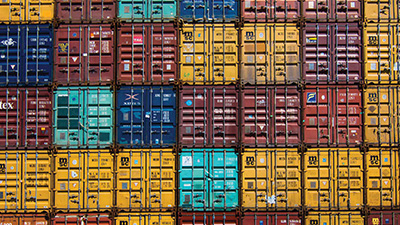 Photograph of shipping containers of different colors, stacked on top of one another like blocks.
