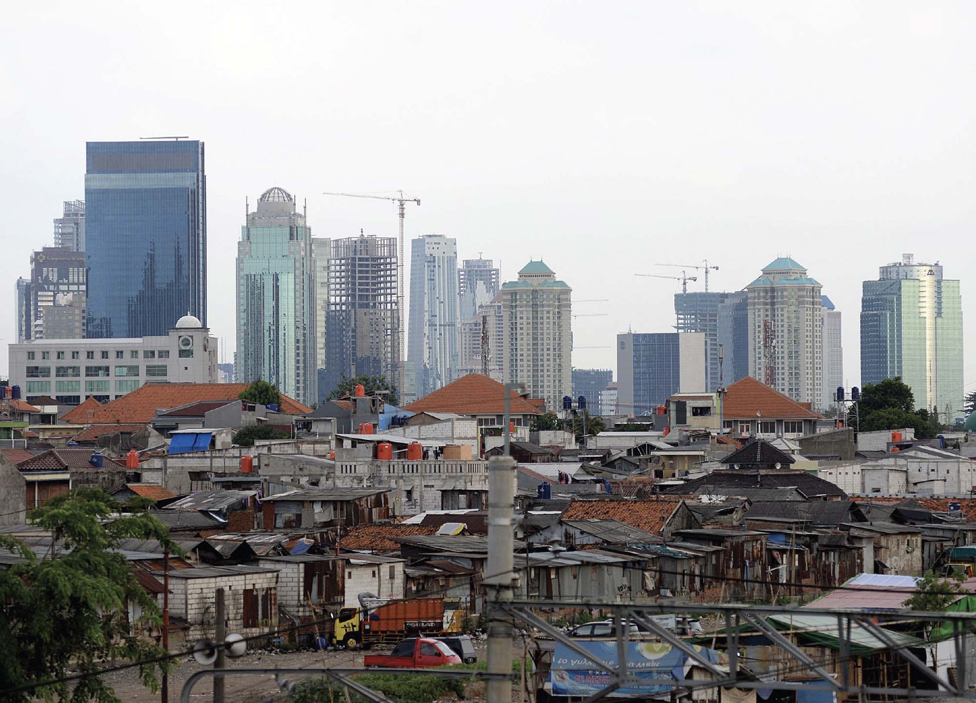 An image that shows a startling contrast: against a skyline of tall, modern buildings, are small, simple brick homes.