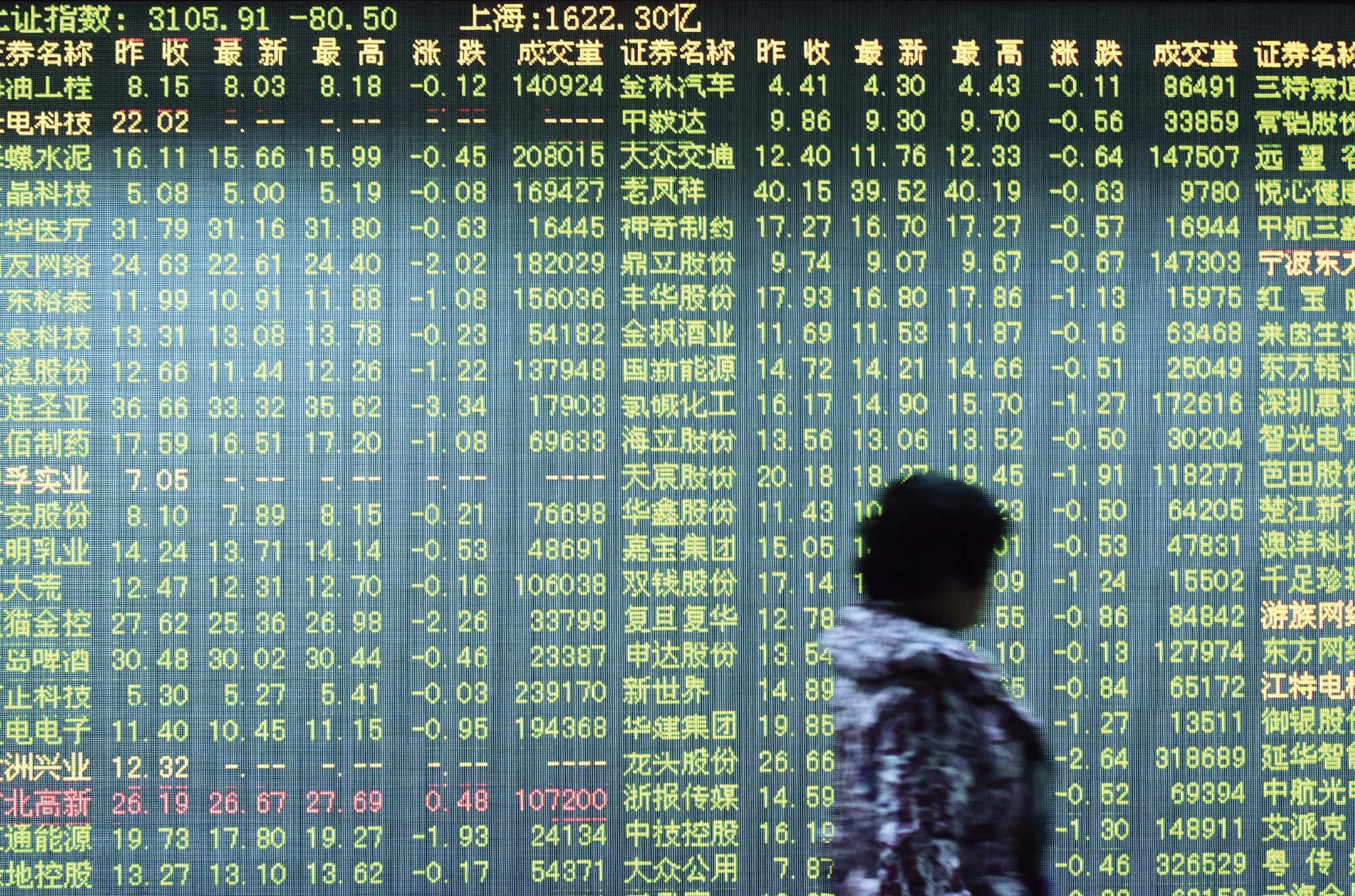 A woman walks past an electronic board showing numbers representing stock market movements.