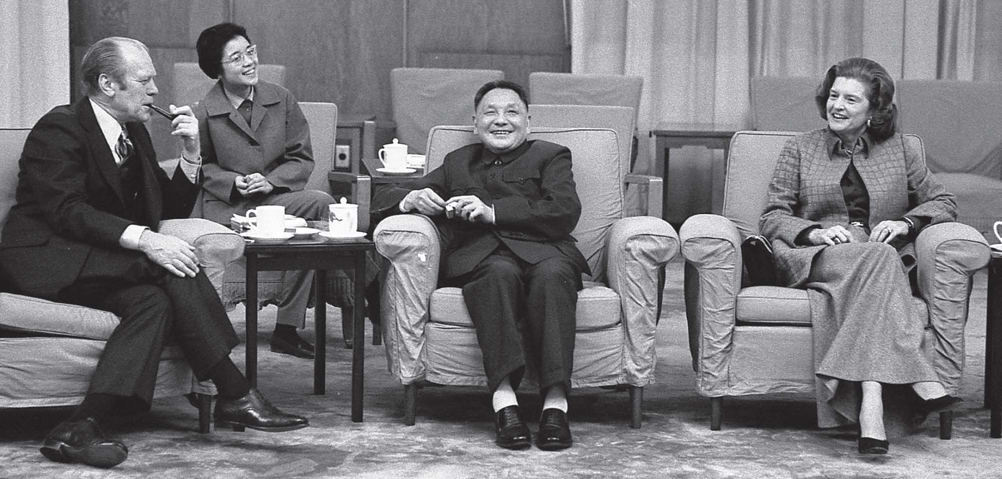 Four people sit in soft armchairs, smiling and drinking tea.