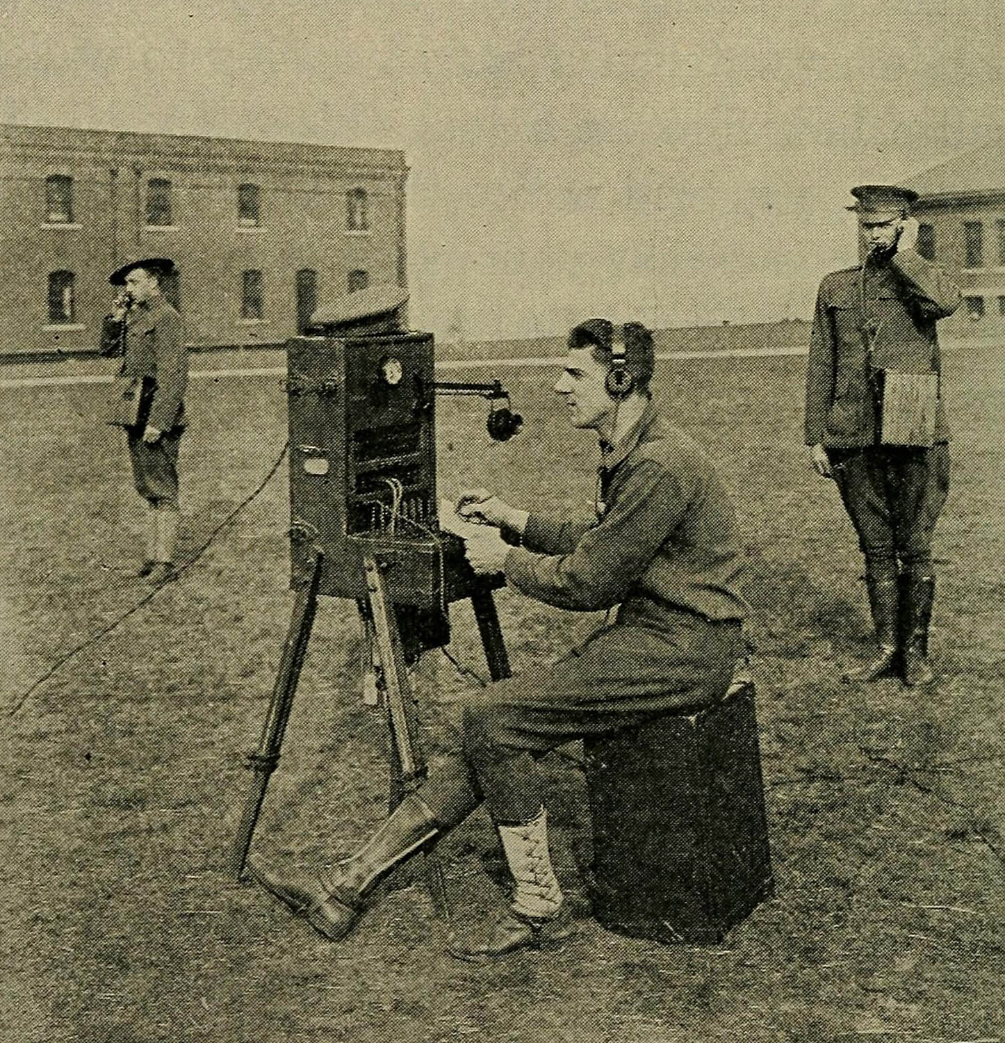 Archival photograph of a solider operating a large field radio with two more soldiers standing in the background with handheld radios.