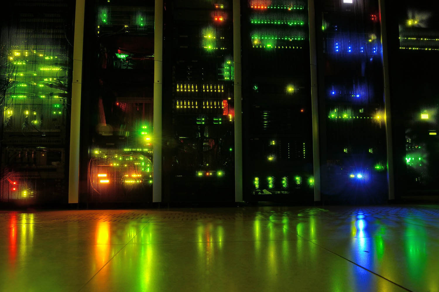 A range of different colored lights illuminate computer servers in a darkened room.