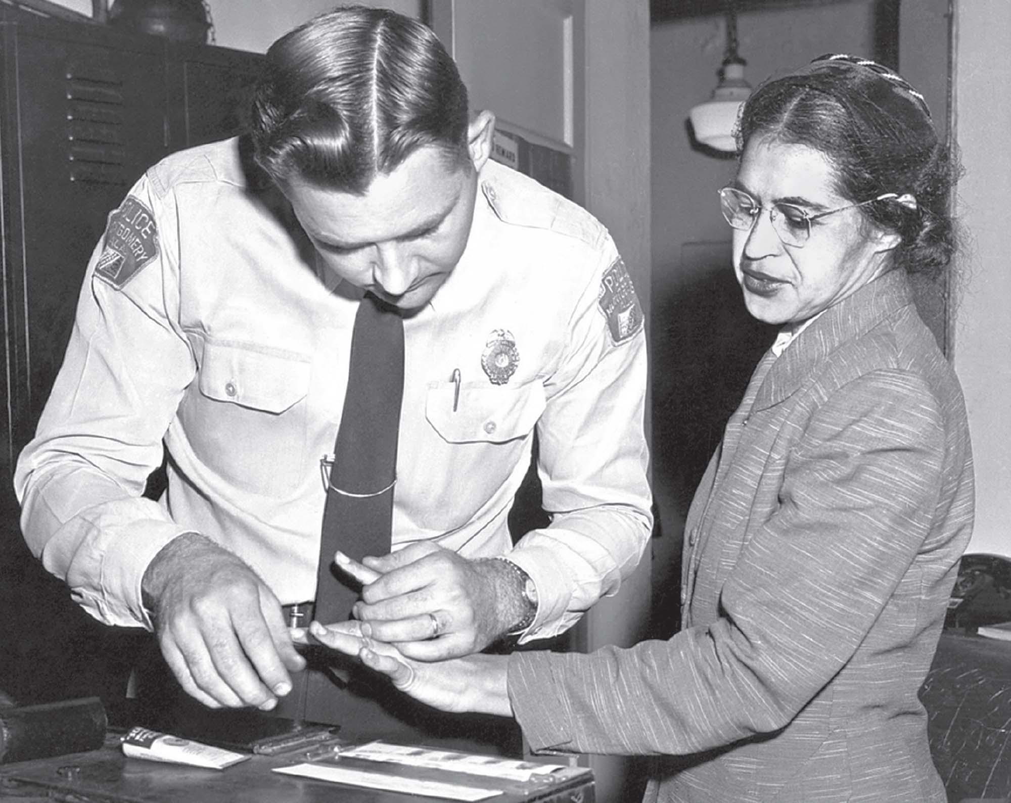 A police officer with Rosa Parks, using ink to take her fingerprints.
